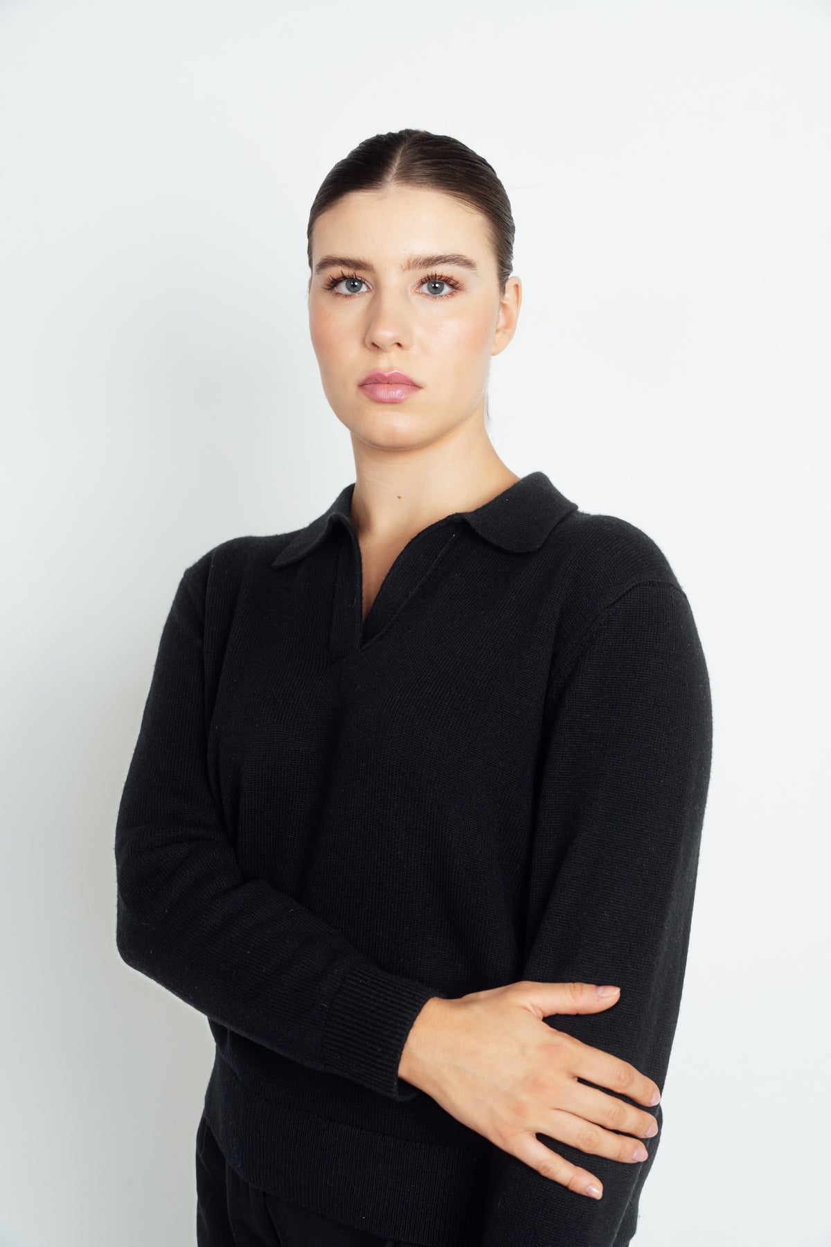 Black Cashmere-Merino Polo Jumper worn with arms folded, showing the open collar and ribbed cuff.