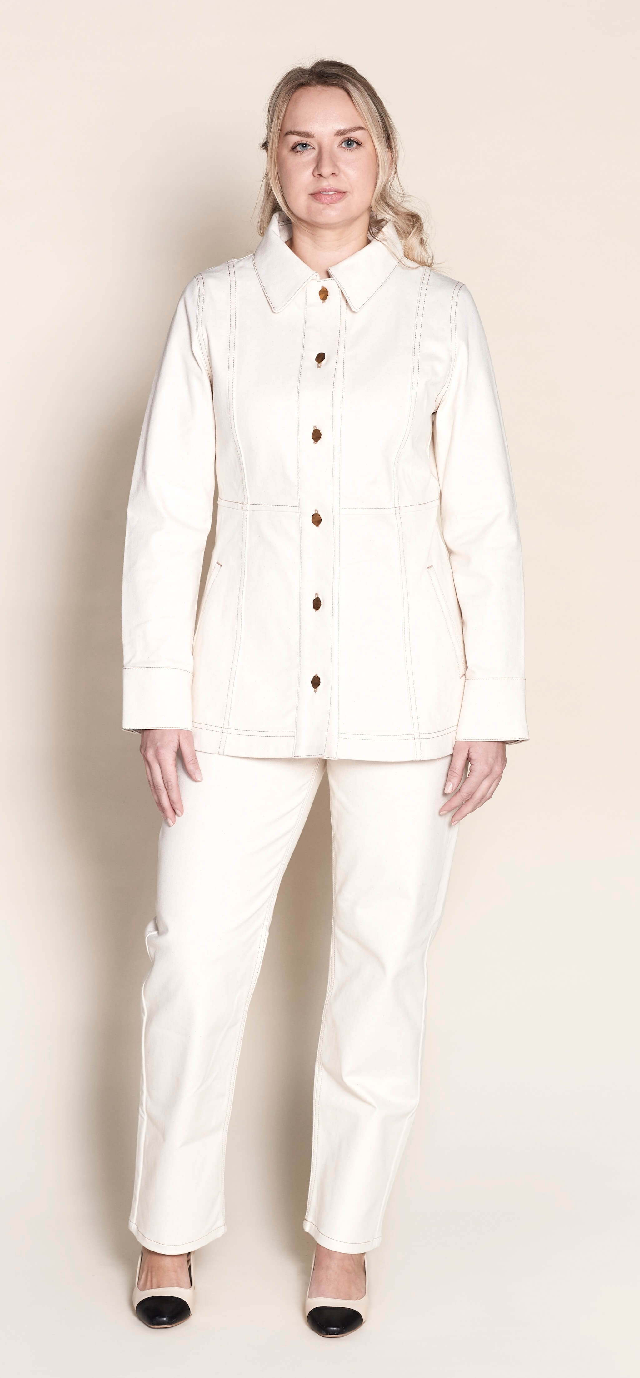 Model stands confidently in Cyme Copenhagen's matching cream denim jacket and trousers set, featuring elegant gold button details, showcasing the timeless appeal and sustainable craftsmanship of Danish design in women's fashion.