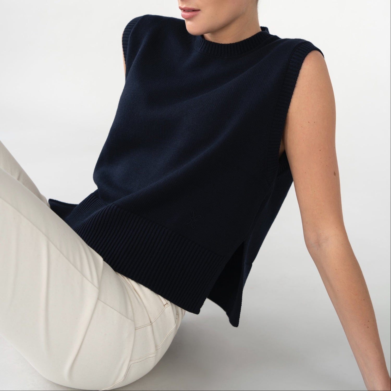 Woman wearing a navy blue sleeveless top sitting on a white surface with a white background