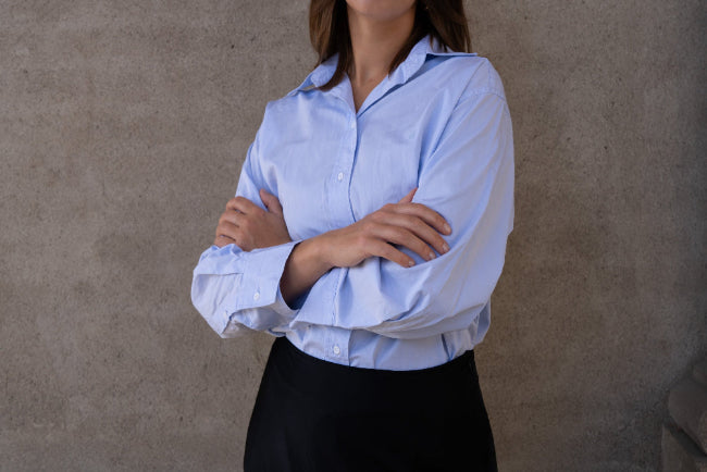 Person wearing a light blue shirt with rolled-up sleeves against a neutral background
