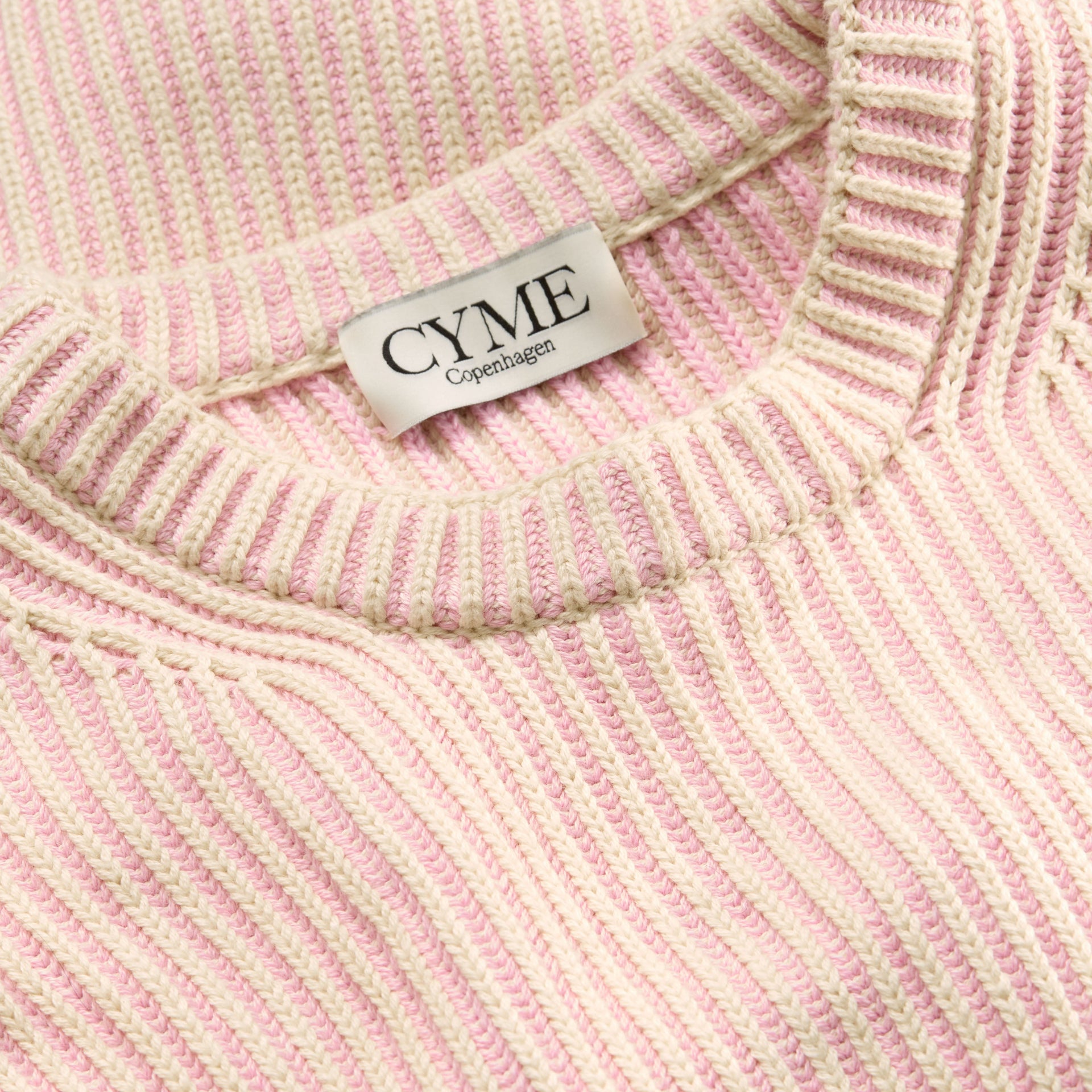 A close-up of the neckline and ribbed texture of a cream and light pink sweater.