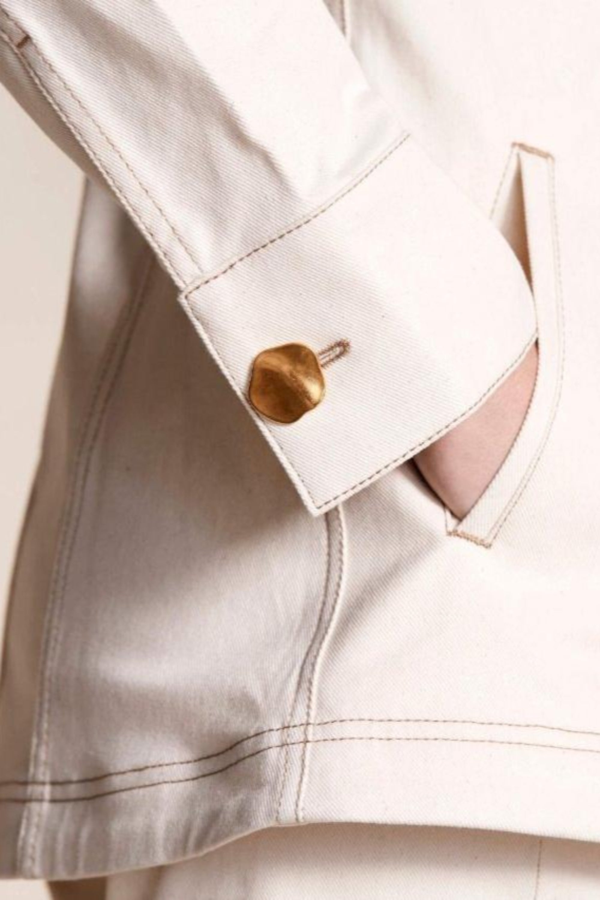 Detail shot of Cyme Copenhagen's cream denim jacket cuff with a unique gold button, showcasing the brand's attention to quality materials and sustainable fashion in women's clothing from a Danish designer.