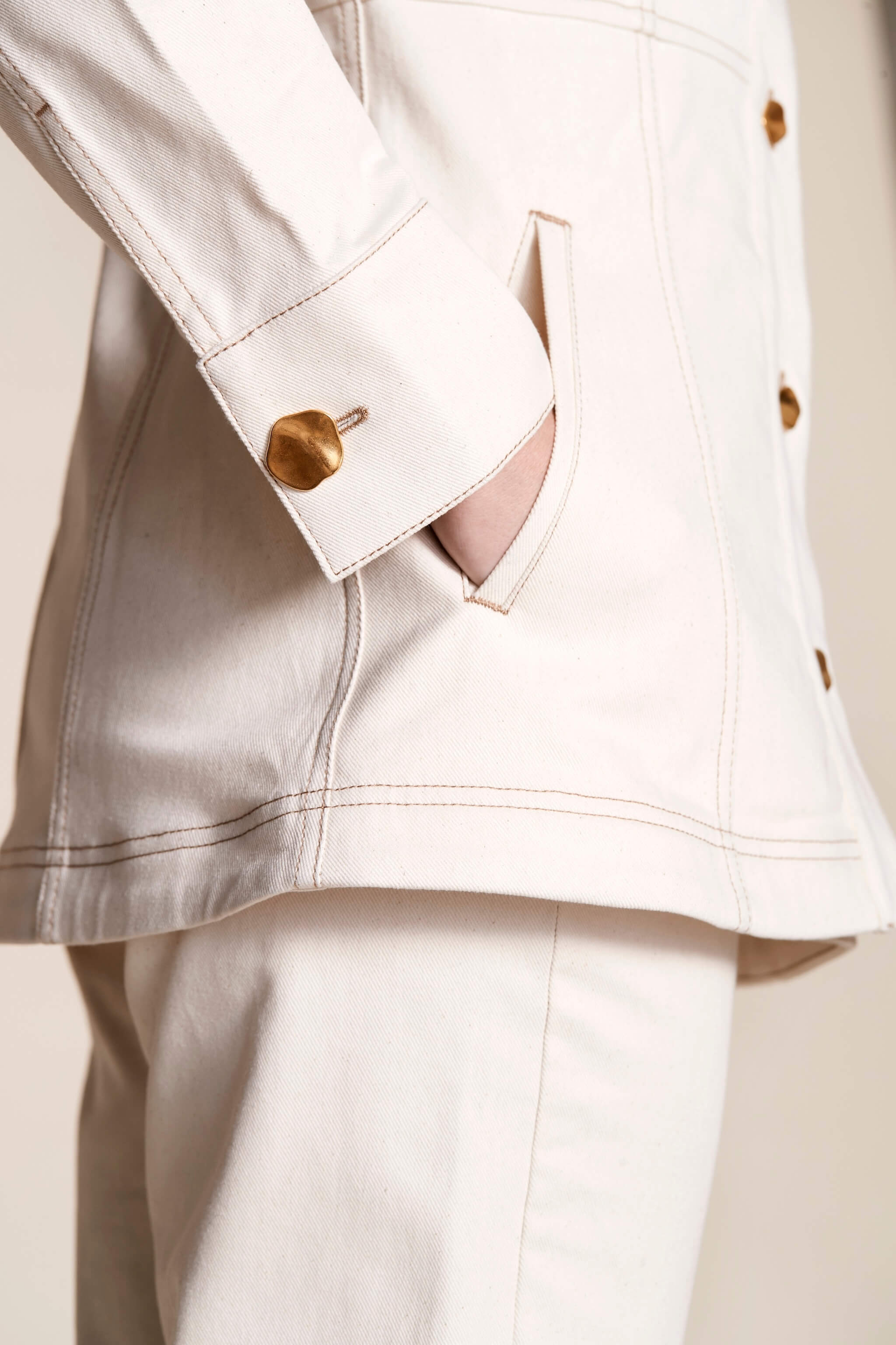 Detail shot of Cyme Copenhagen's cream denim jacket cuff with a unique gold button, showcasing the brand's attention to quality materials and sustainable fashion in women's clothing from a Danish designer.