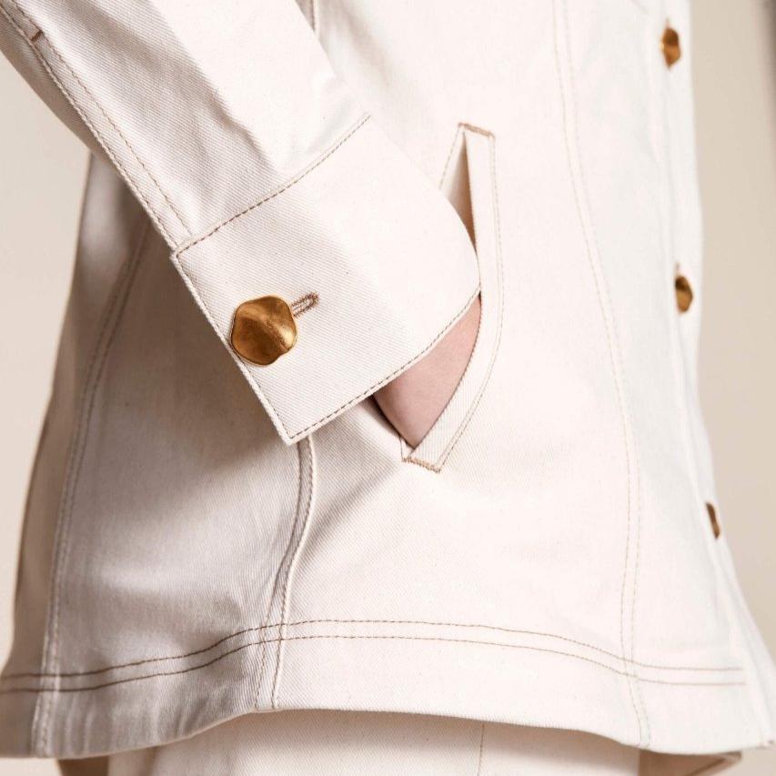 Detail shot of Cyme Copenhagen's cream denim jacket cuff with a unique gold button, showcasing the brand's attention to quality materials and sustainable fashion in women's clothing from a Danish designer.