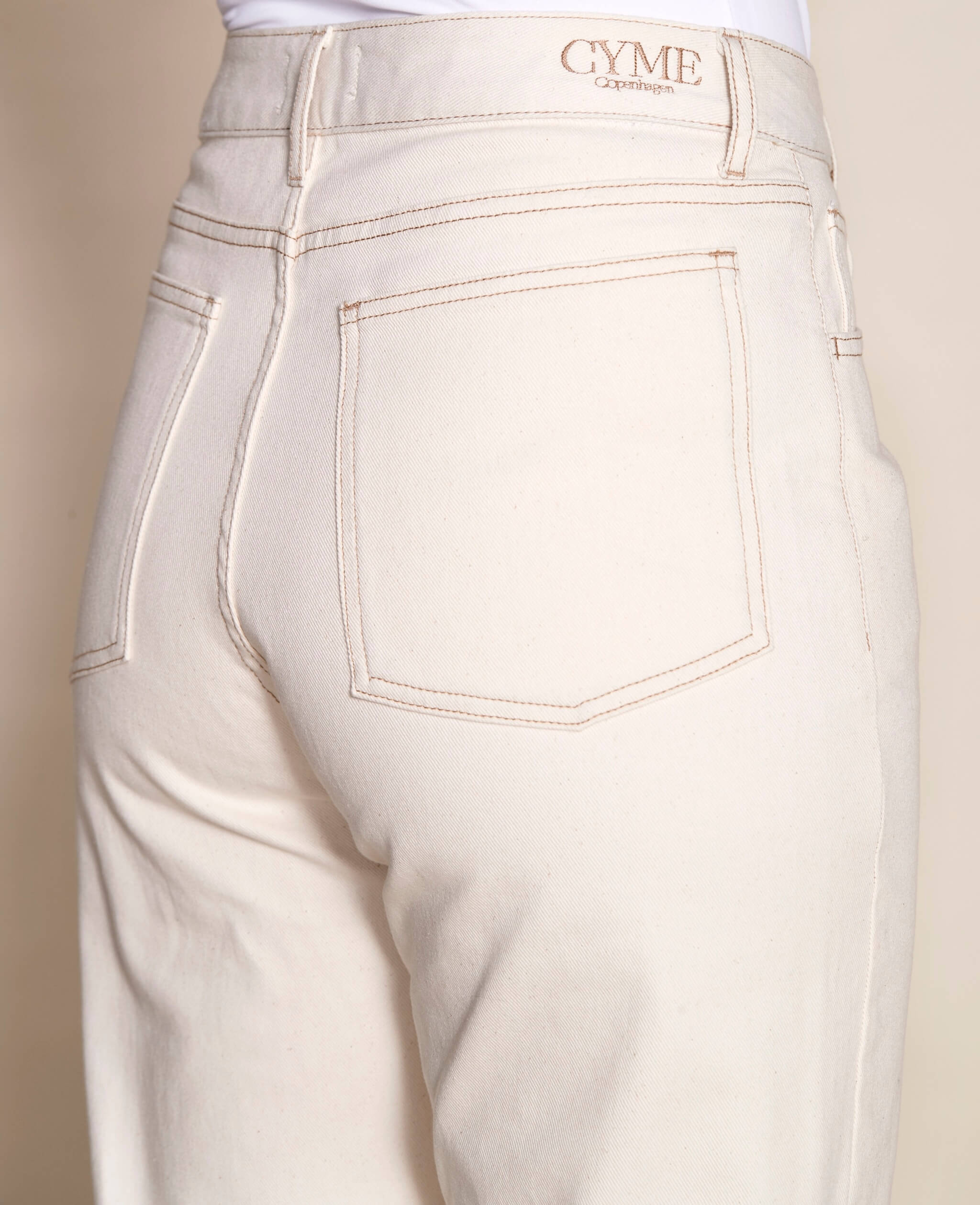 Detail of Cyme Copenhagen's cream denim pants, focusing on the back pocket with branded tag, emphasizing the brand's quality craftsmanship and ethical fashion standards in Denmark's clothing shops.