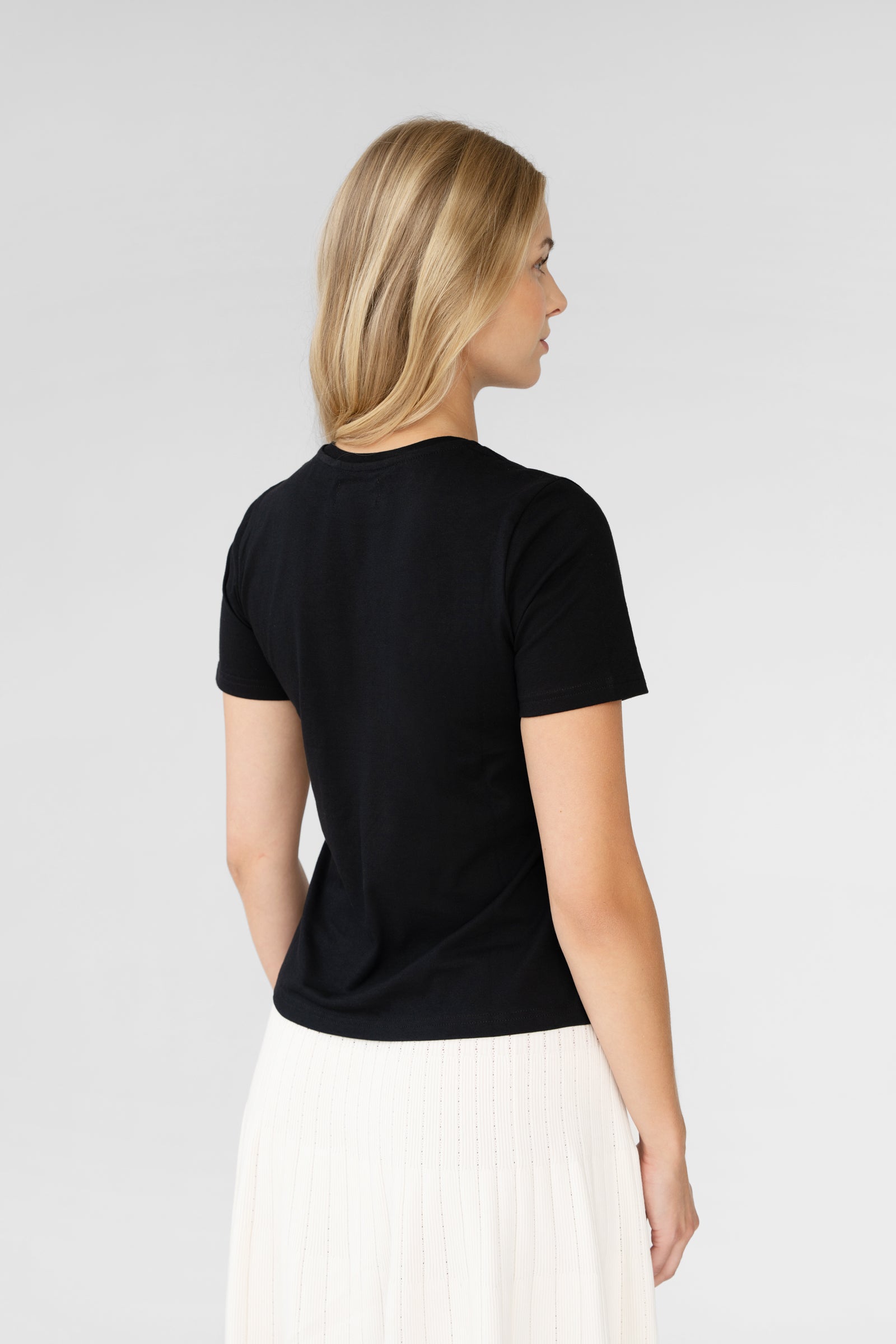 Woman wearing a black t-shirt and white pants on a light gray background