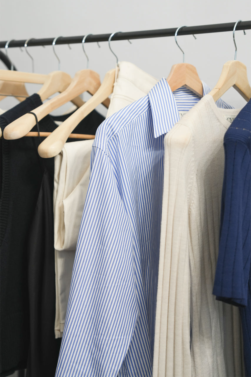 Clothing items including shirts and a sweater on hangers against a neutral background
