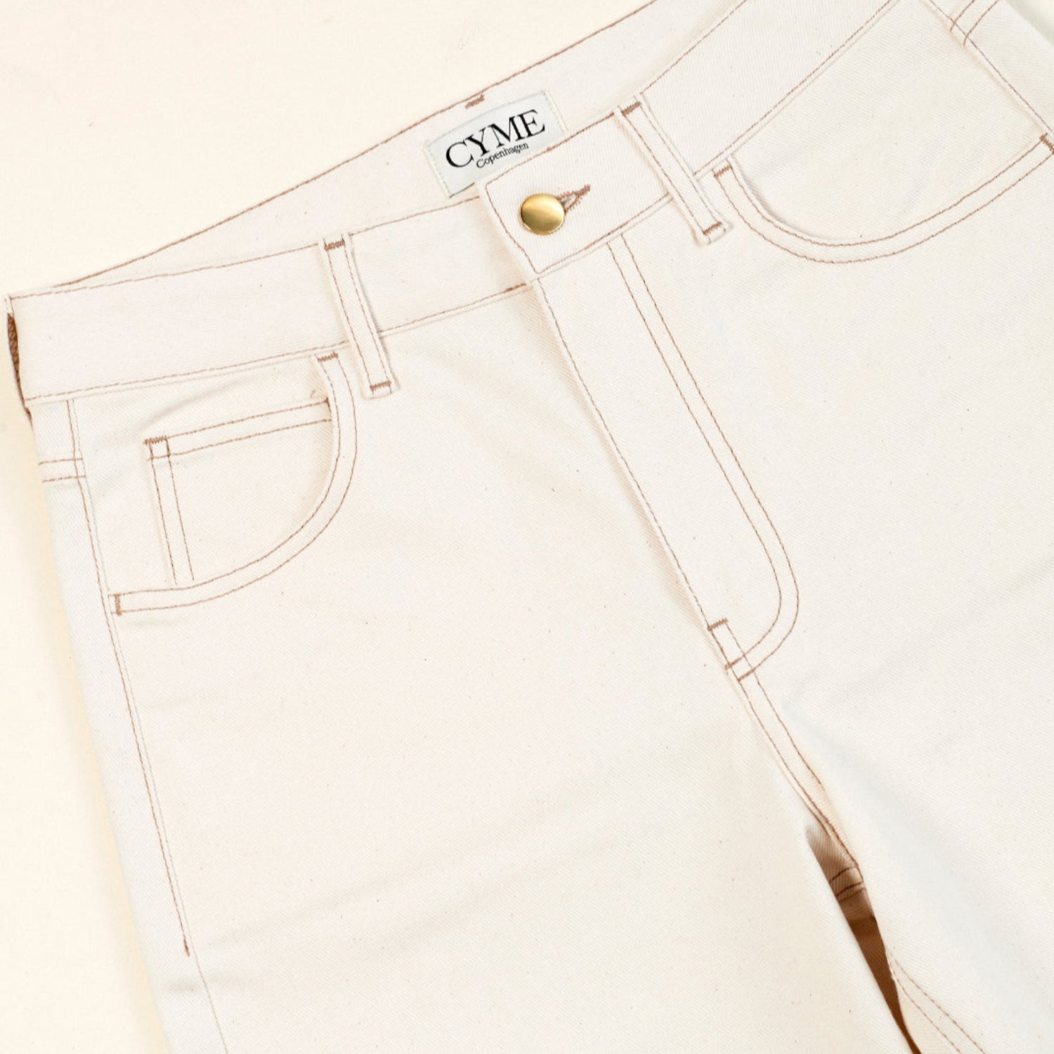 White jeans with a brand logo on a light beige background