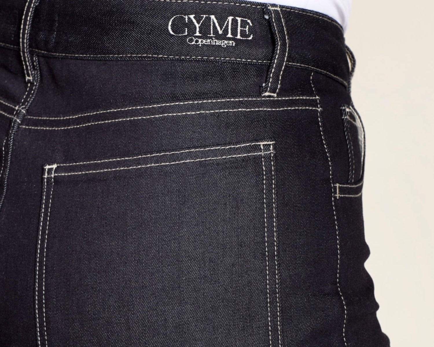 Black jeans with 'CYME Copenhagen' branding on a beige background