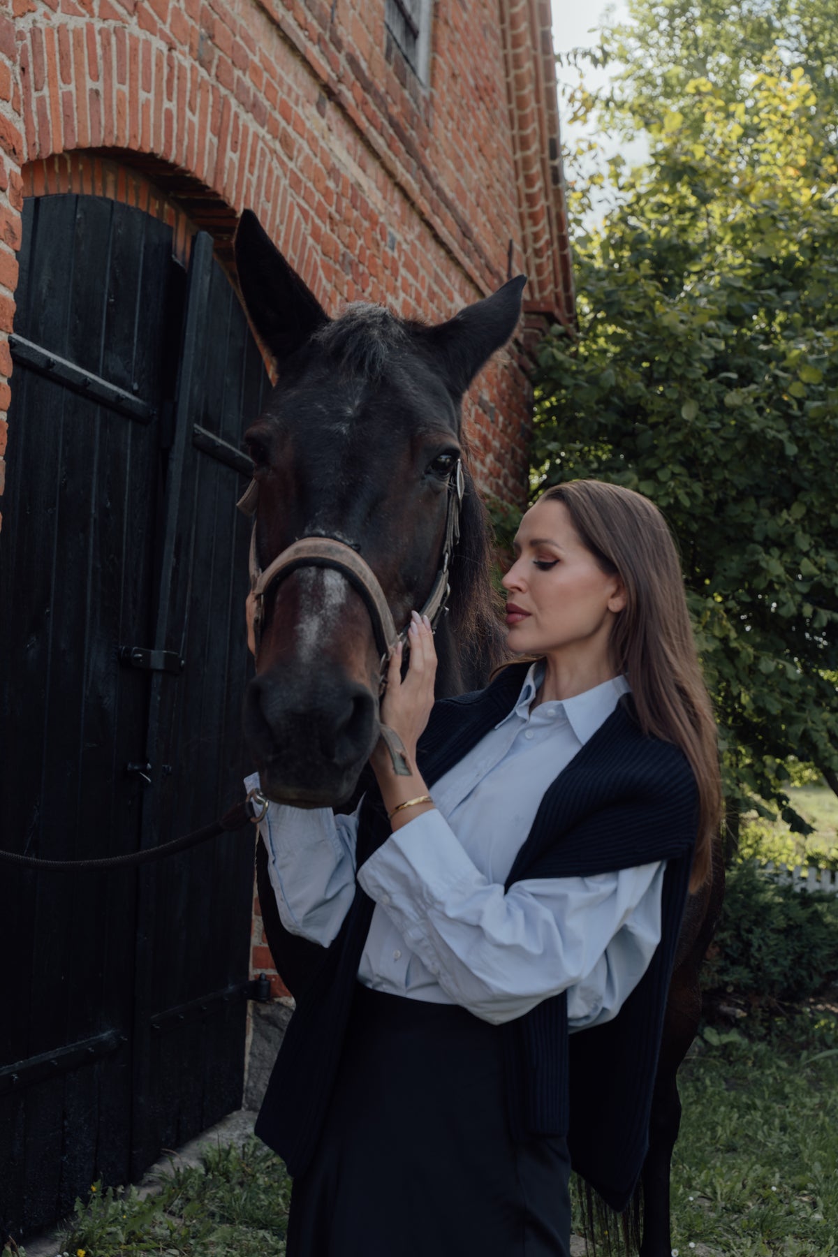 Light blue Cyme Supima Shirt styled with a dark knit over the shoulders, photographed beside a horse.