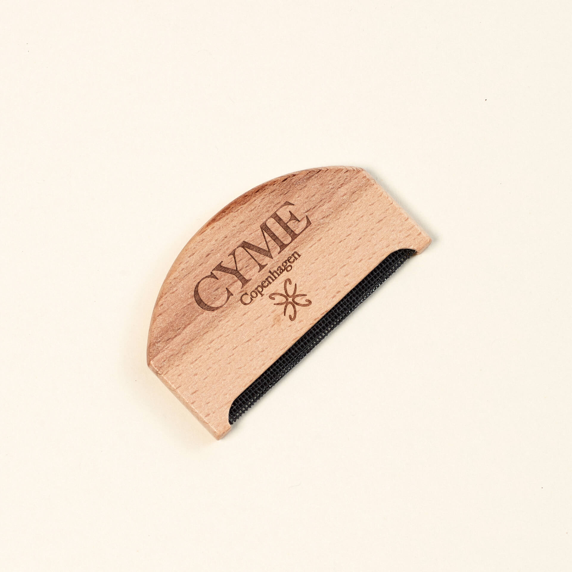 Close-up of a wooden garment comb from CYME Copenhagen. The comb features the CYME Copenhagen logo and branding engraved on the wood, with a fine black mesh edge for removing lint and pilling from clothing.