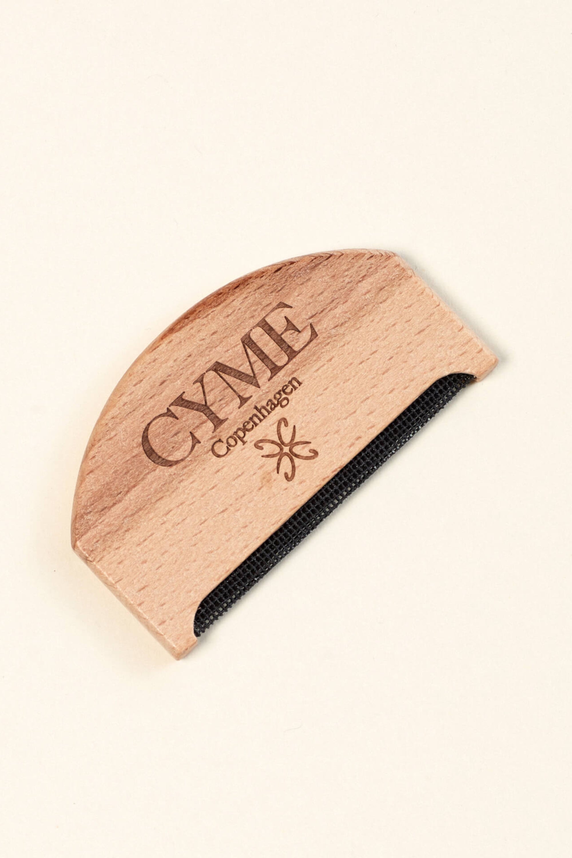 Close-up of a wooden garment comb from CYME Copenhagen. The comb features the CYME Copenhagen logo and branding engraved on the wood, with a fine black mesh edge for removing lint and pilling from clothing.