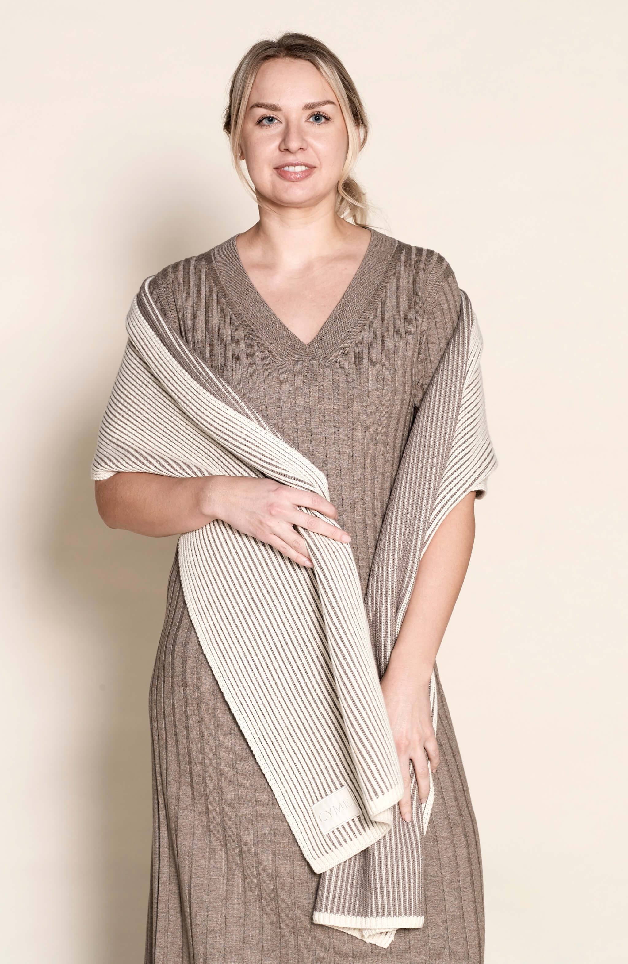 Model draped in a Cyme Copenhagen luxurious cashmere knit dress paired with a contrasting striped scarf, showcasing the fusion of natural materials and timeless fashion in Danish design.