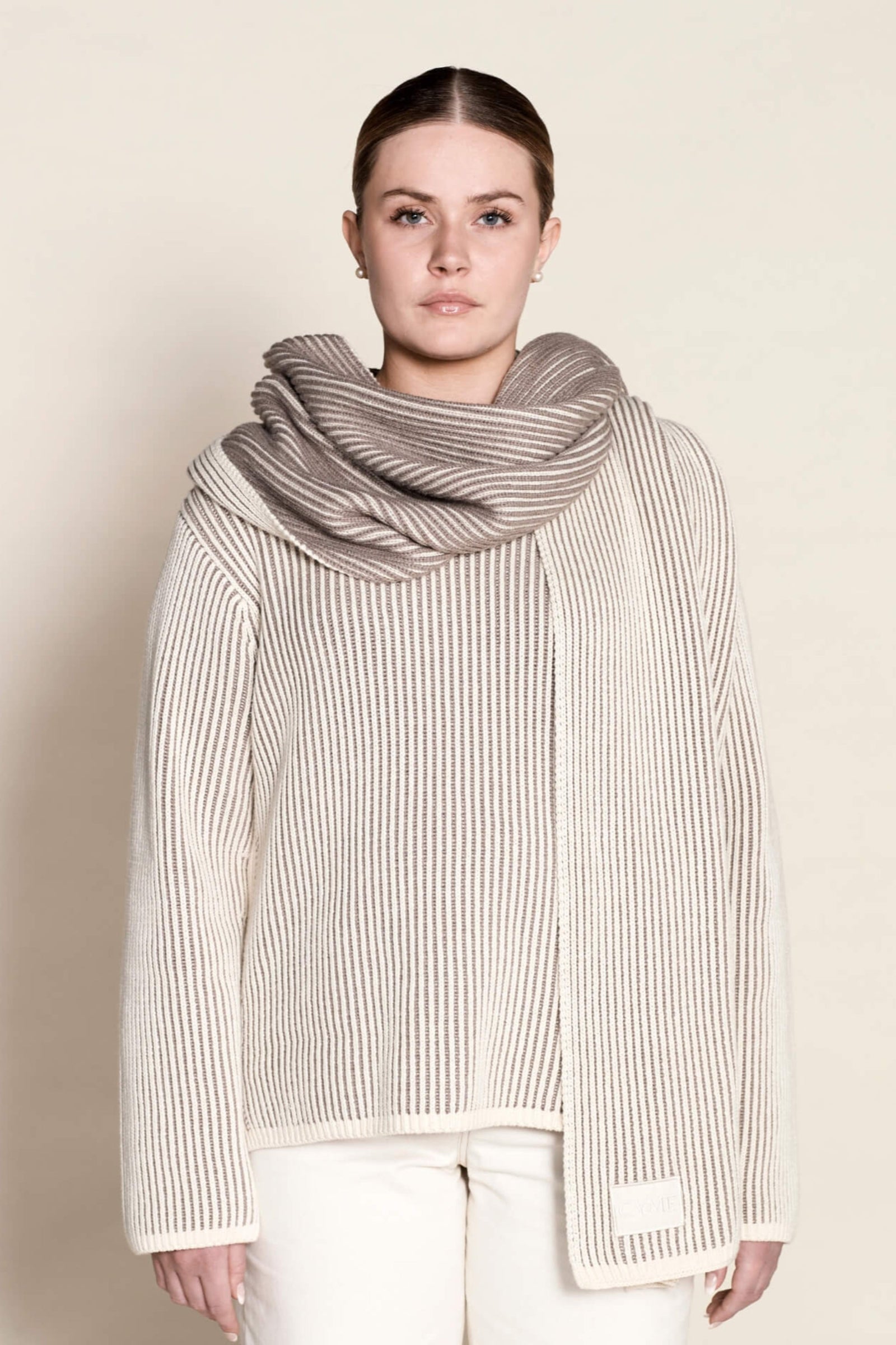 A model poses in Cyme Copenhagen's elegant cashmere knit sweater in cream, paired with a matching luxurious scarf, exemplifying the brand's commitment to sustainable fashion and natural materials.