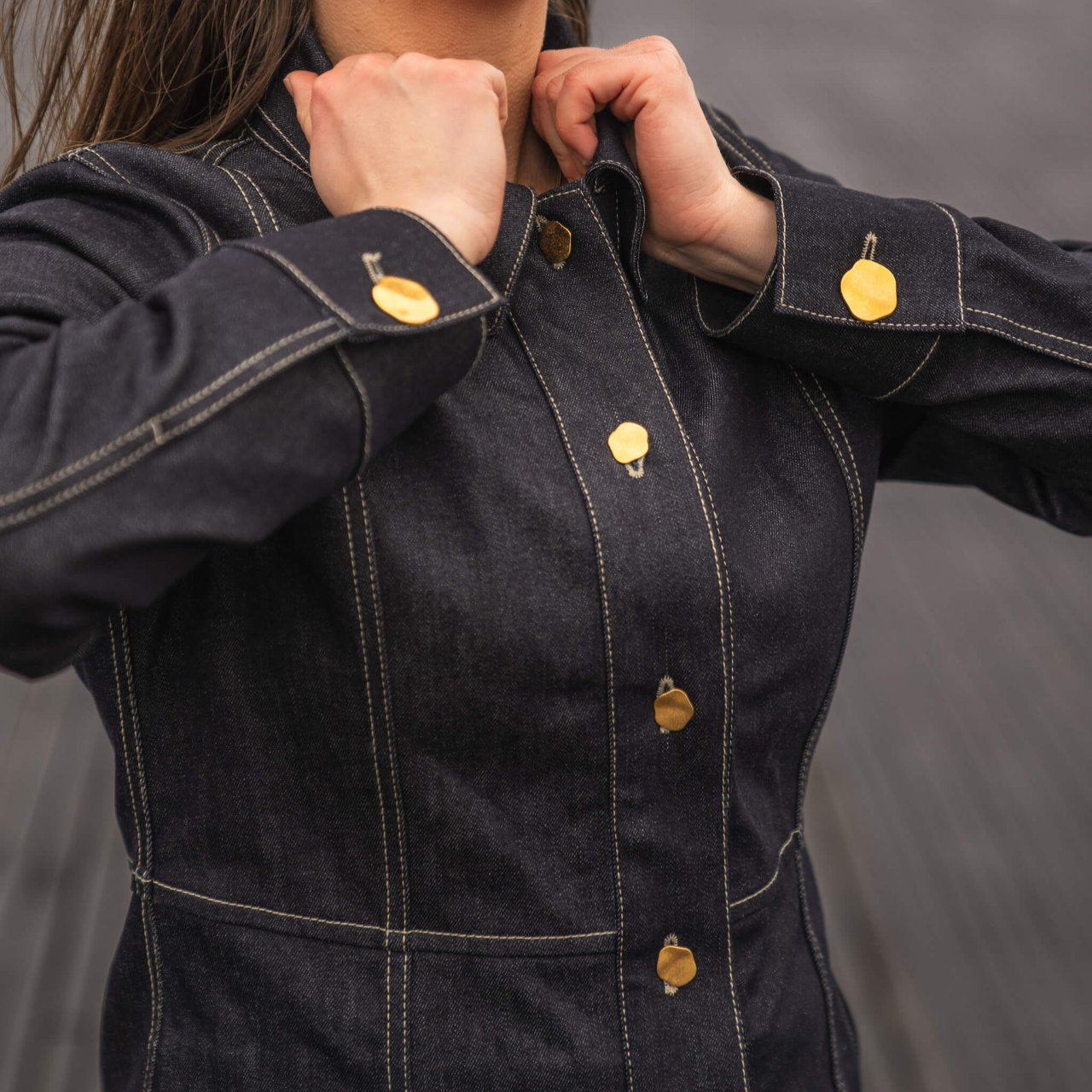 Close-up of a woman adjusting a Cyme Copenhagen dark denim jacket with distinctive gold button detailing, highlighting the brand's commitment to durable materials and timeless design in women's clothing.