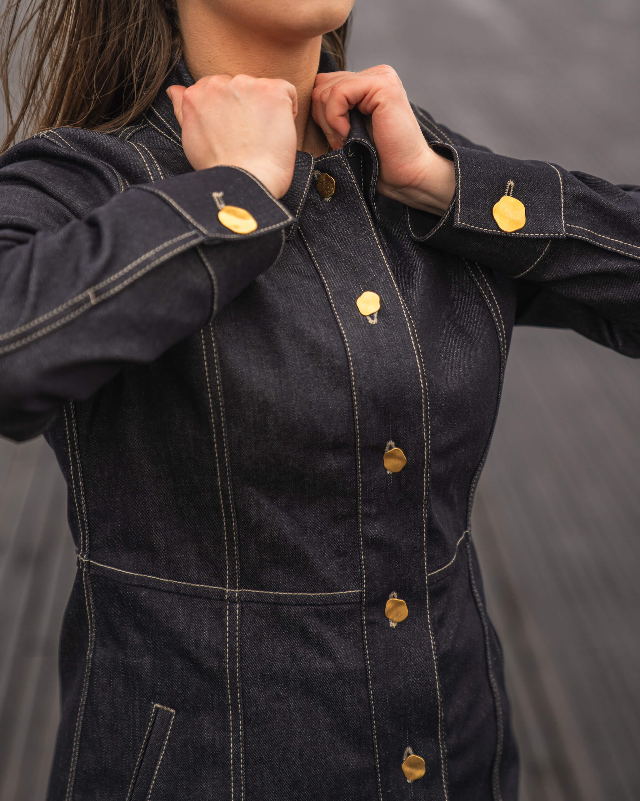 Close-up of a woman adjusting a Cyme Copenhagen dark denim jacket with distinctive gold button detailing, highlighting the brand's commitment to durable materials and timeless design in women's clothing.