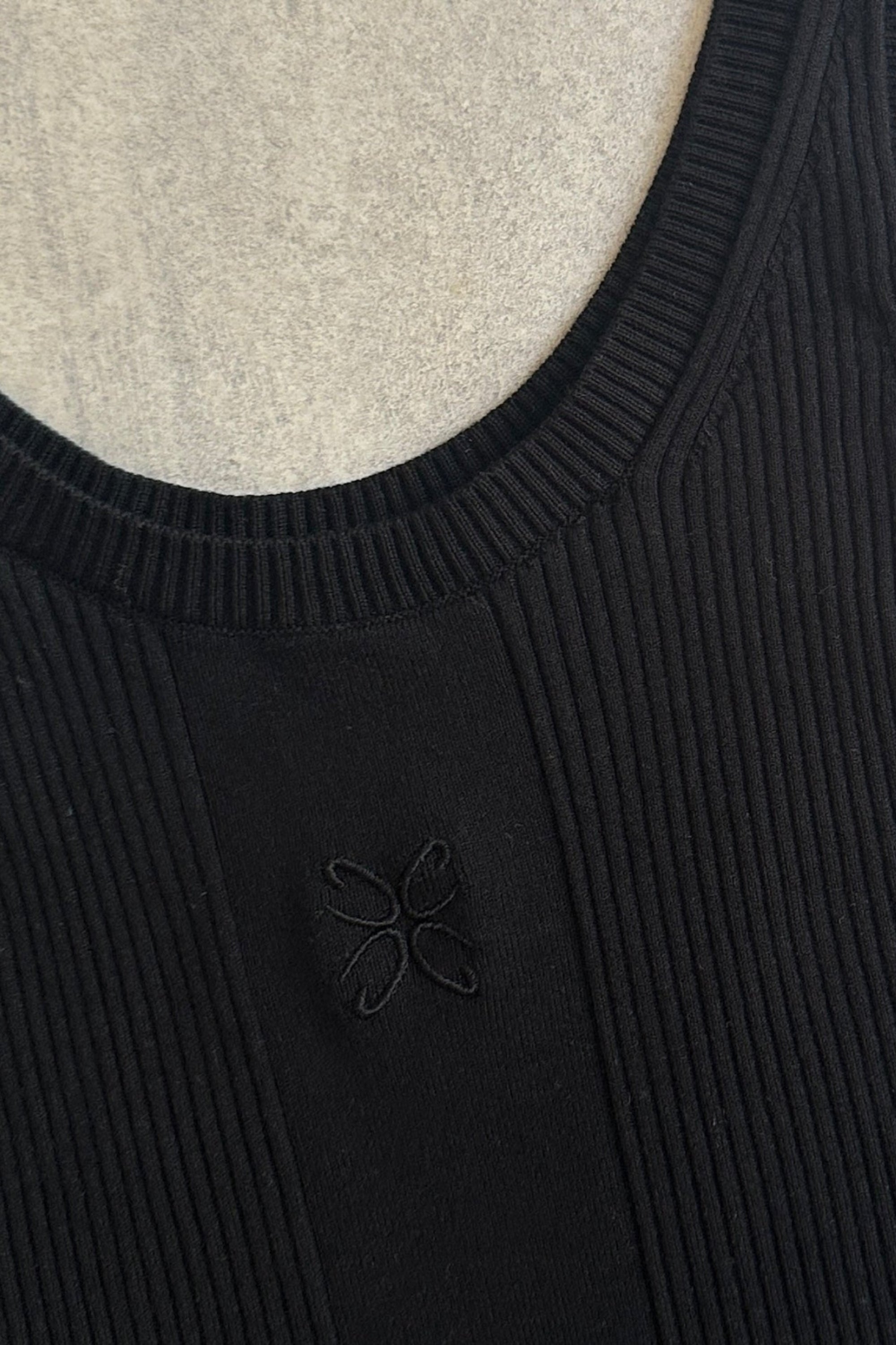 Nærbillede af ribstrikket tanktop fra CYME Copenhagen i sort med broderet logo på brystet. Fremstillet i blød viskoseblanding med rund hals og brede stropper.