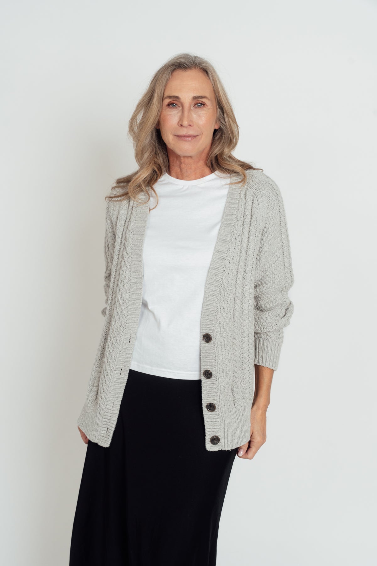 Front view of the grey Hazel Cable Knit Cardigan worn open over a white T-shirt, with dark buttons and cable-knit panels.