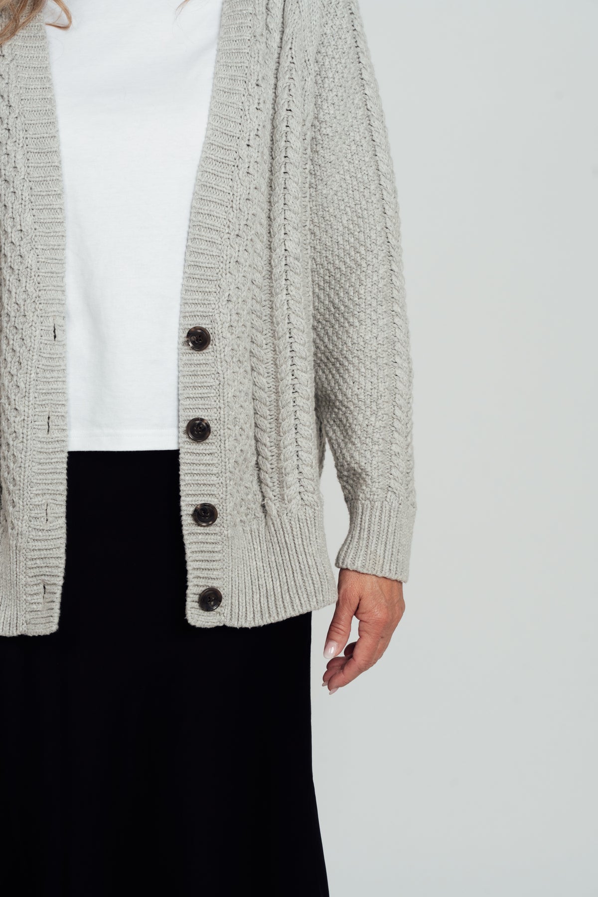 Detail of the grey Hazel Cable Knit Cardigan's dark buttons, cable-knit front, ribbed hem and cuff.