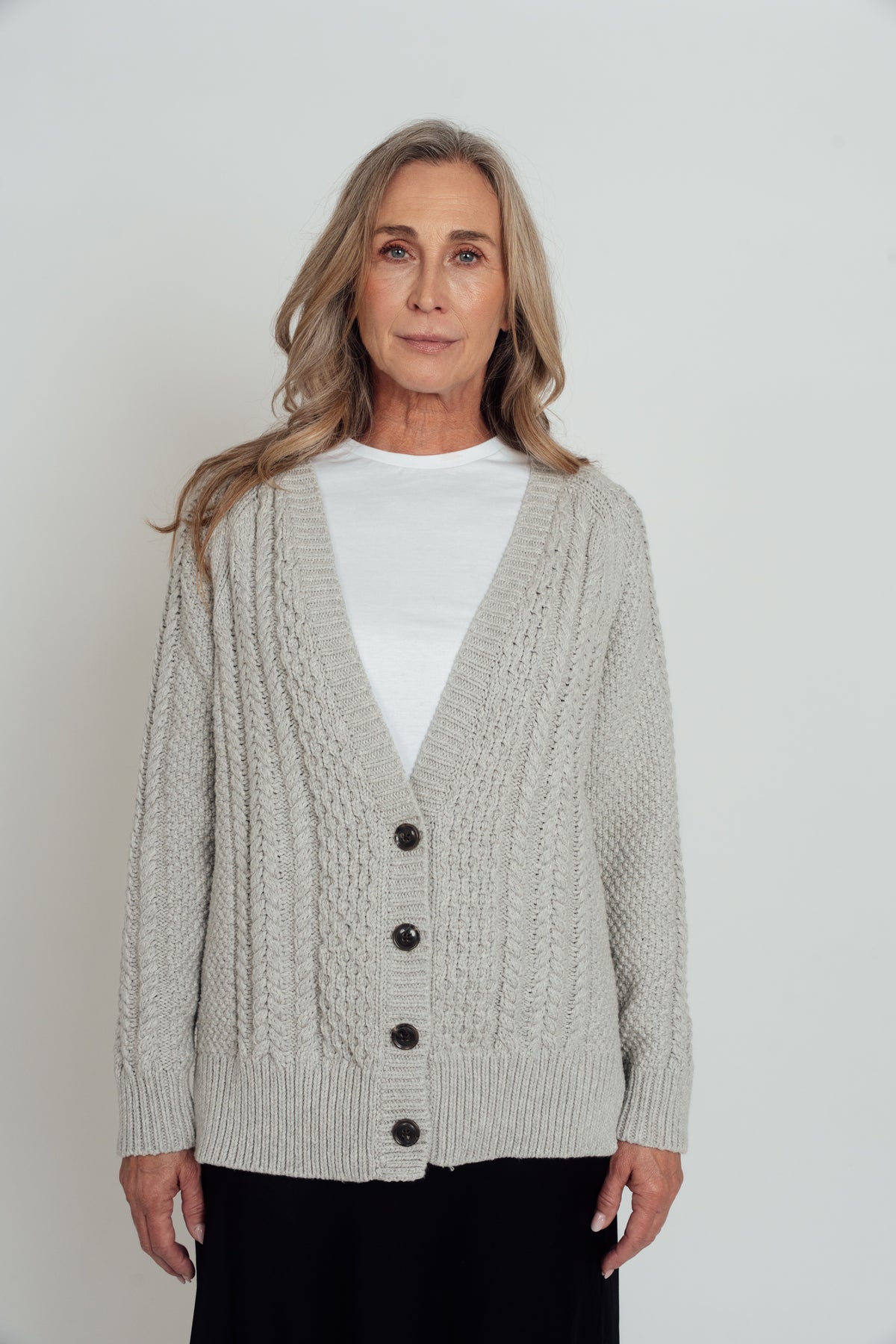 Front view of the grey Hazel Cable Knit Cardigan buttoned over a white T-shirt, showing its V-neck and ribbed hem.