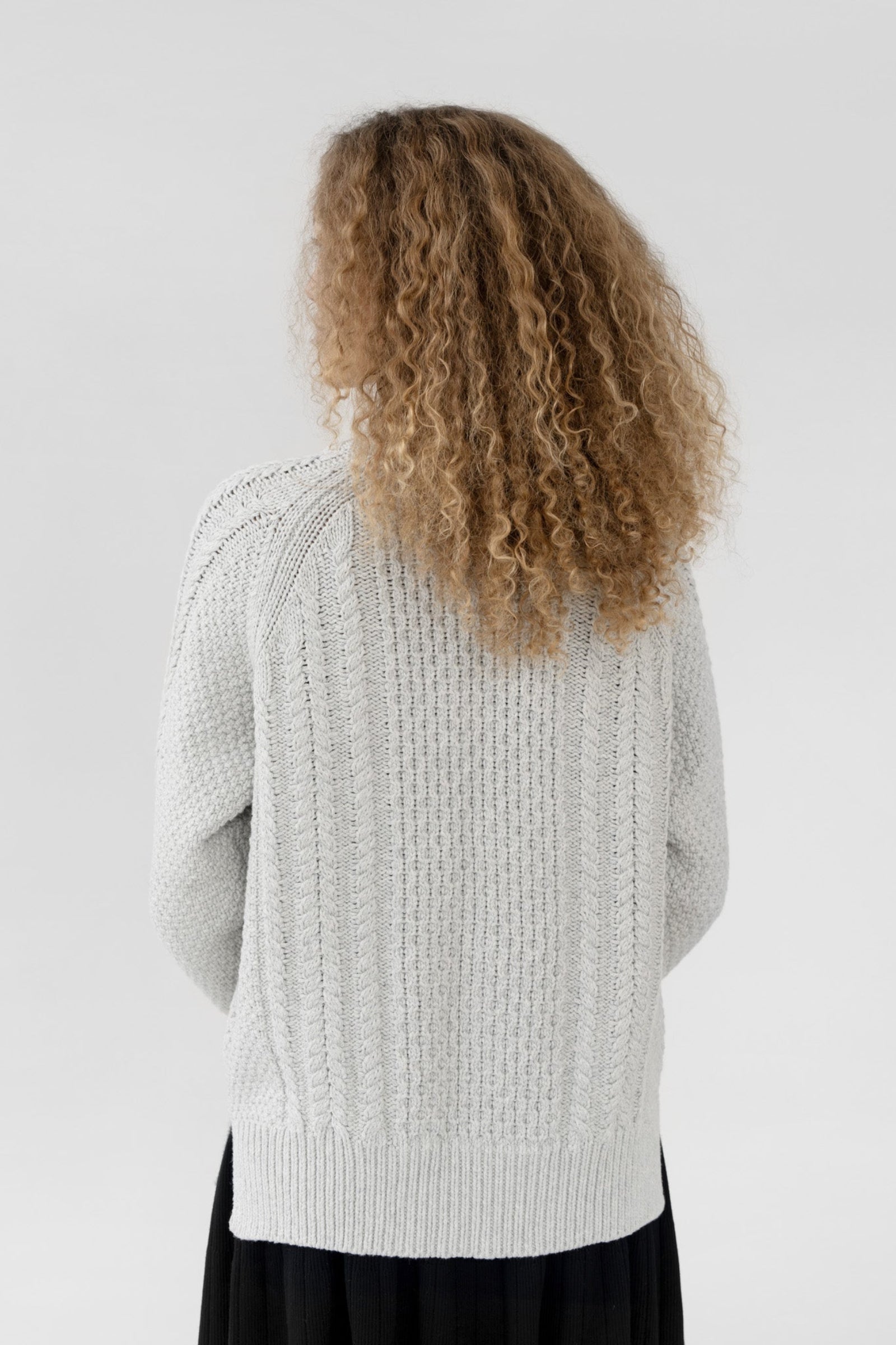 Person wearing a light gray knitted sweater with a plain background