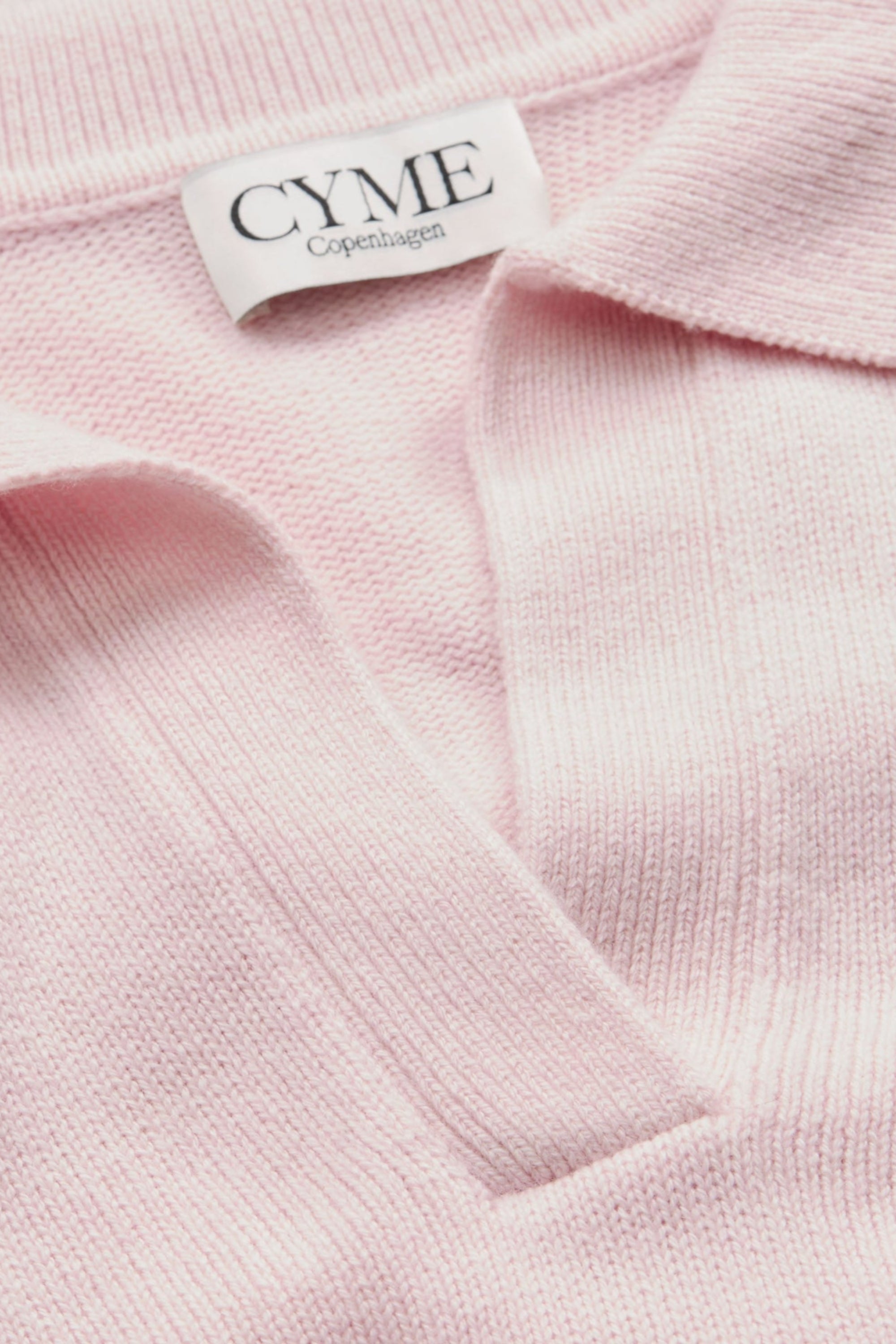 A close-up of the collar and neckline of a light pink polo-style knit jumper, featuring a "CYME Copenhagen" label.