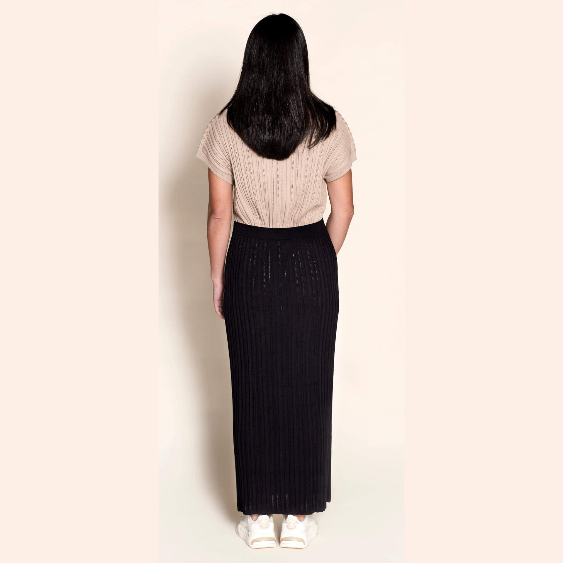 Back view of a model in Cyme Copenhagen attire, pairing a taupe ribbed knit top with a black knit skirt, highlighting the brand's fusion of comfort and Danish designer fashion in sustainable women's clothing.