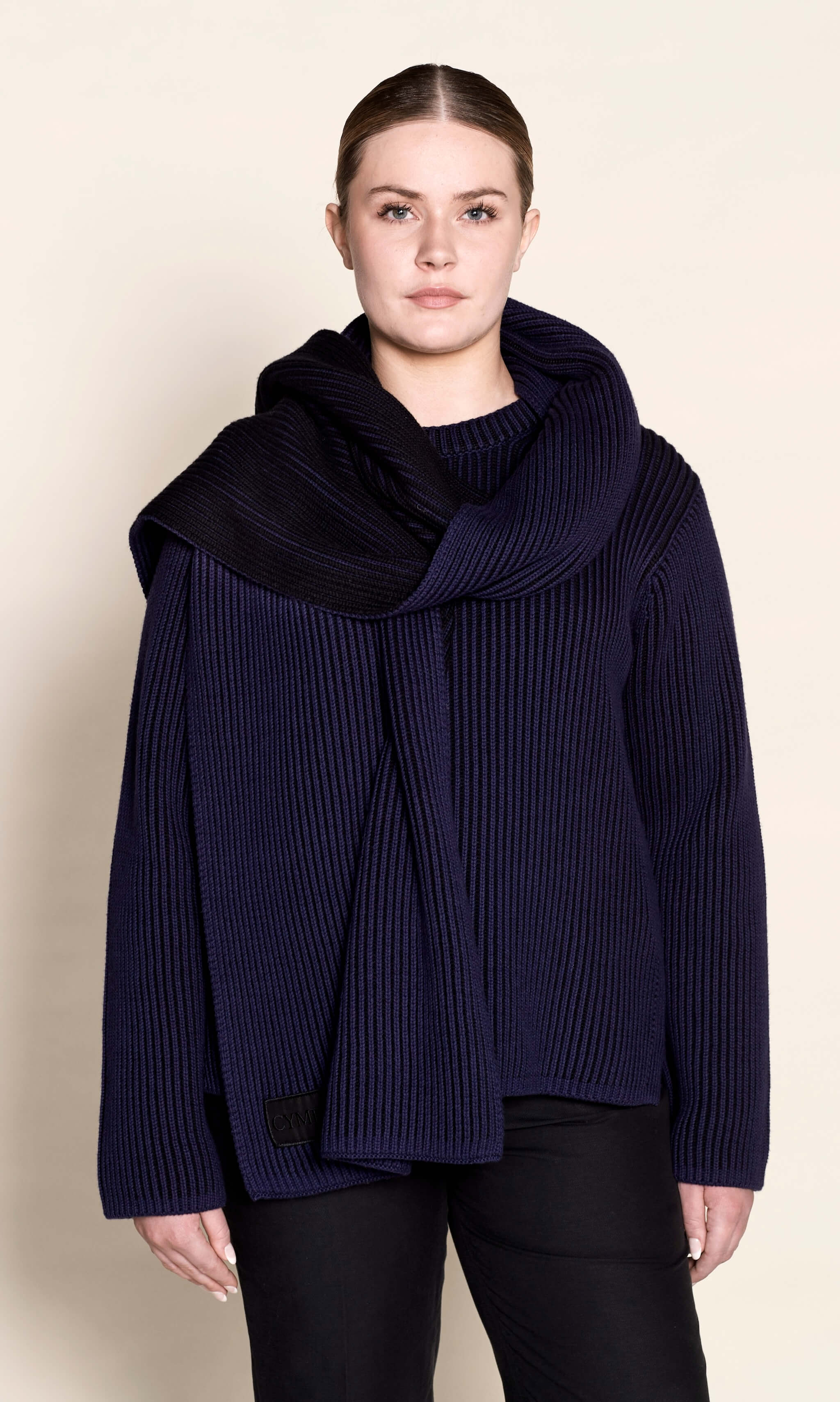 Model draped in Cyme Copenhagen's navy ribbed knit scarf paired with a matching sweater, showcasing the luxurious, sustainable materials used by the Danish fashion brand in their women's clothing line.