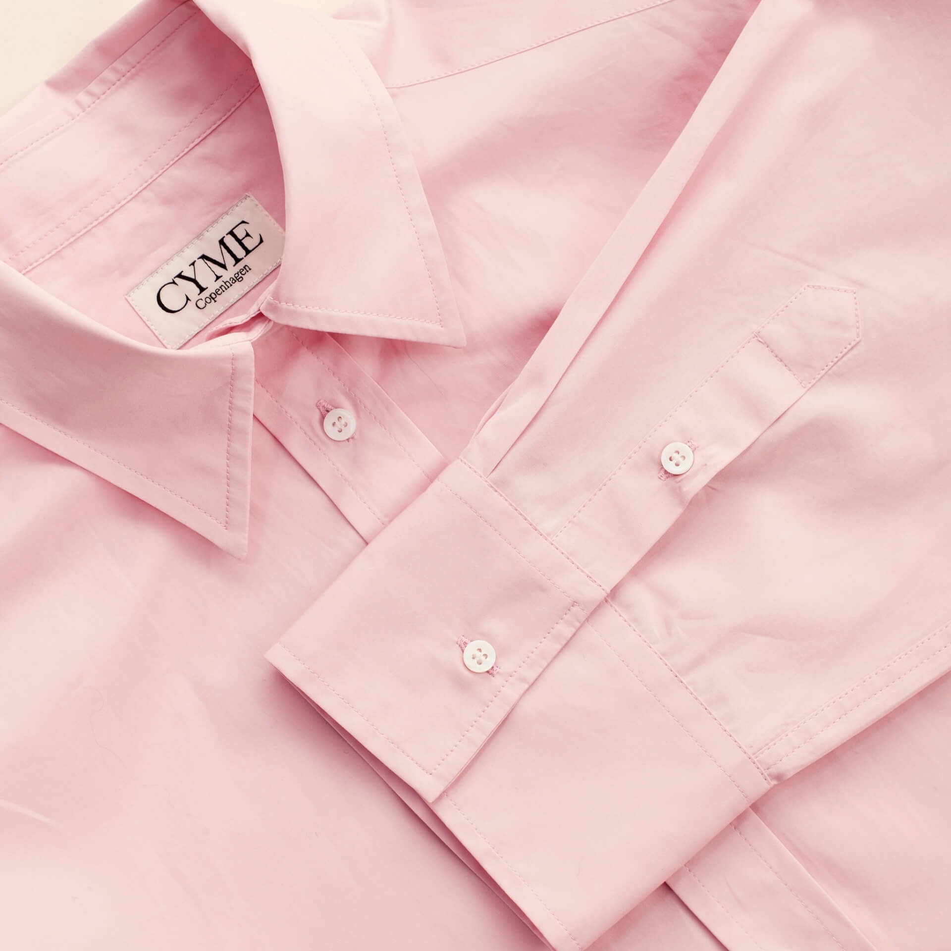 Detail of a delicate pink supima cotton shirt by Cyme Copenhagen, showcasing the brand's label, precision stitching, and commitment to sustainable fashion materials, encapsulating the ethos of a top Danish designer in women's clothing.