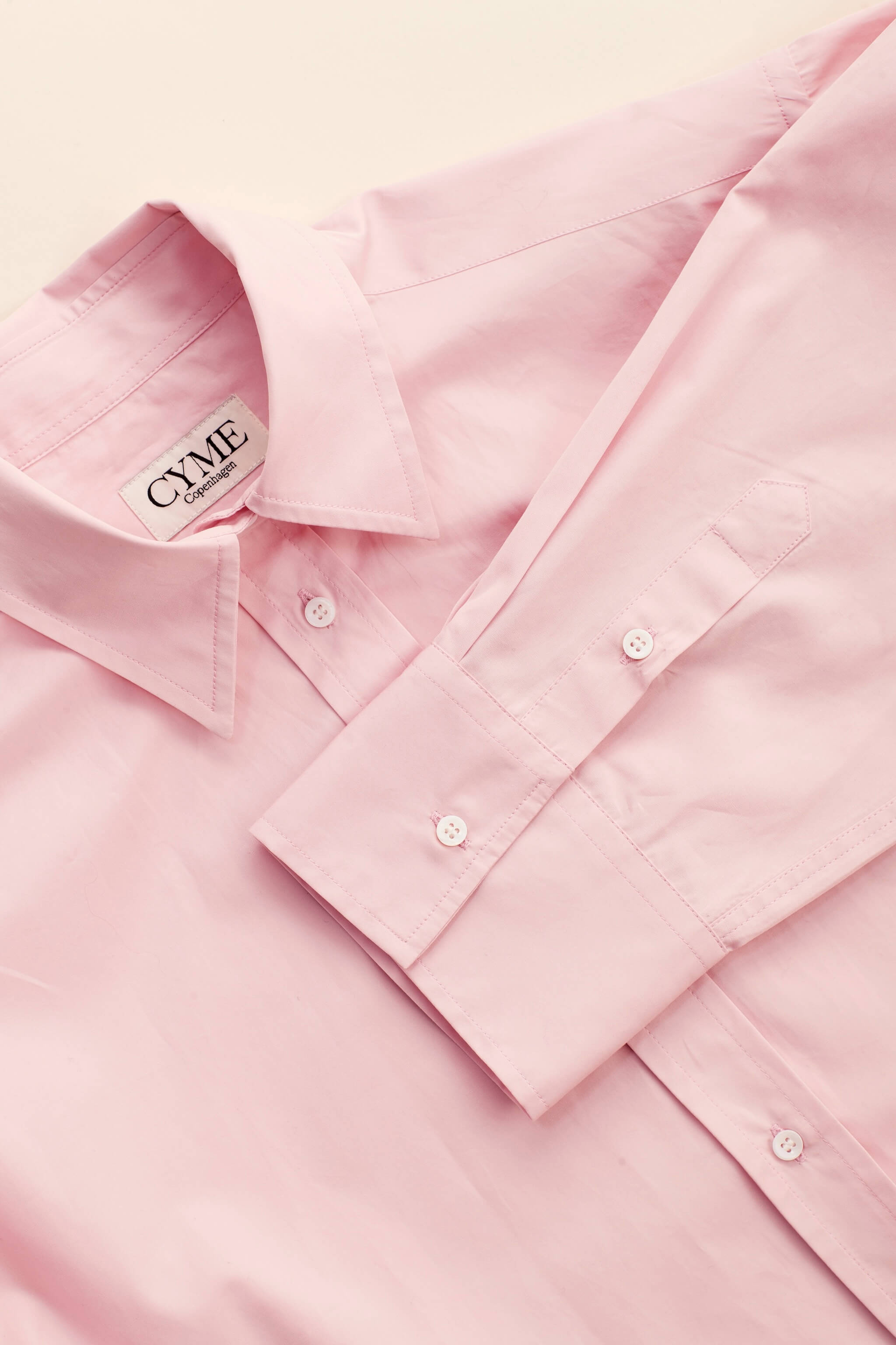 Detail of a delicate pink supima cotton shirt by Cyme Copenhagen, showcasing the brand's label, precision stitching, and commitment to sustainable fashion materials, encapsulating the ethos of a top Danish designer in women's clothing.
