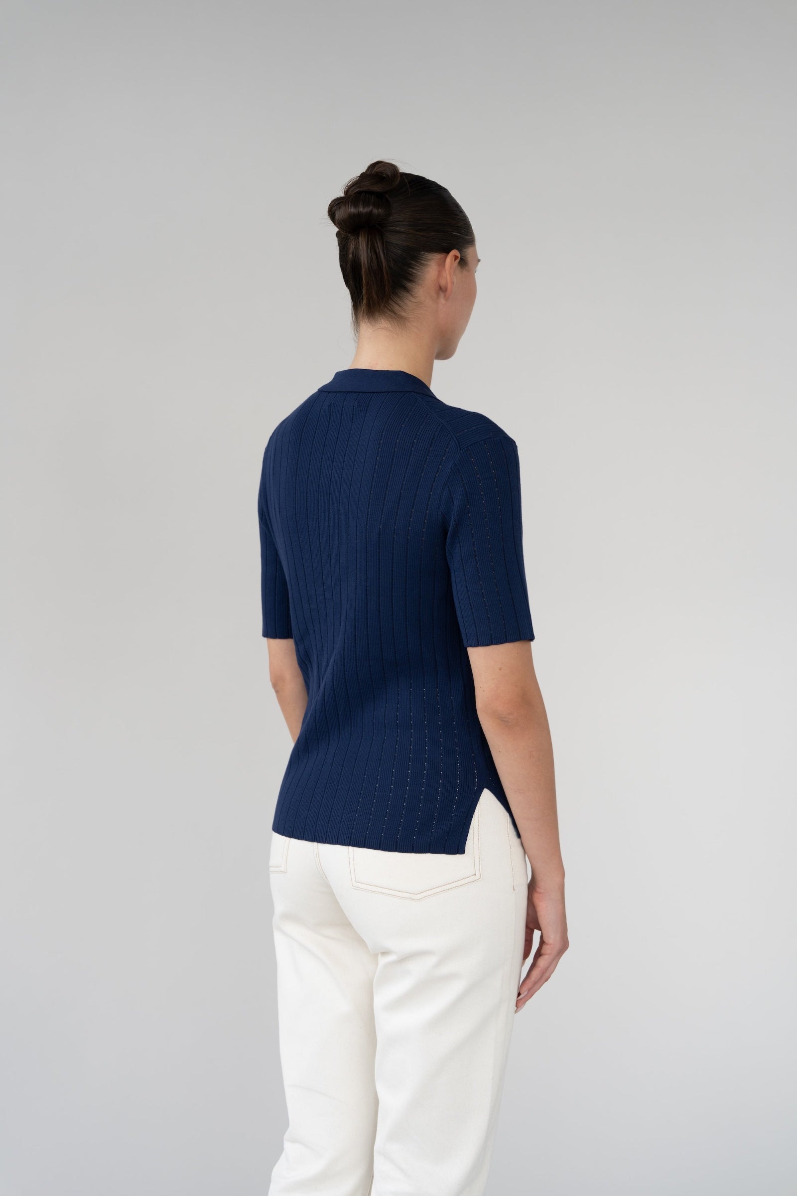 Person wearing a navy blue shirt and white pants on a light gray background