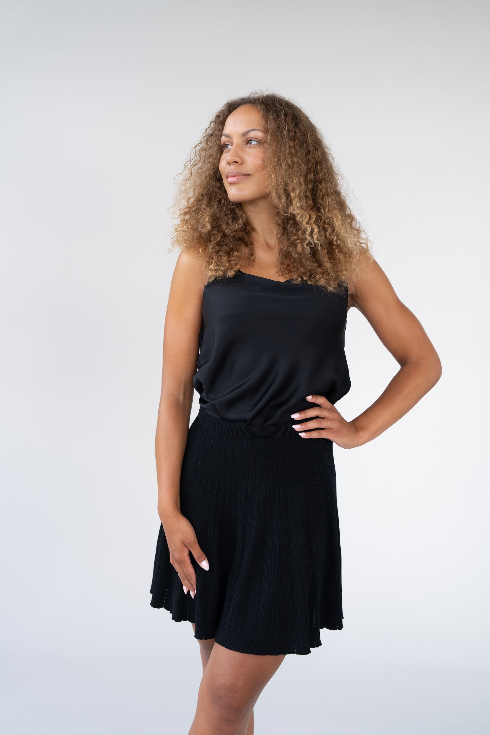 Woman wearing a black top and satin skirt against a white background