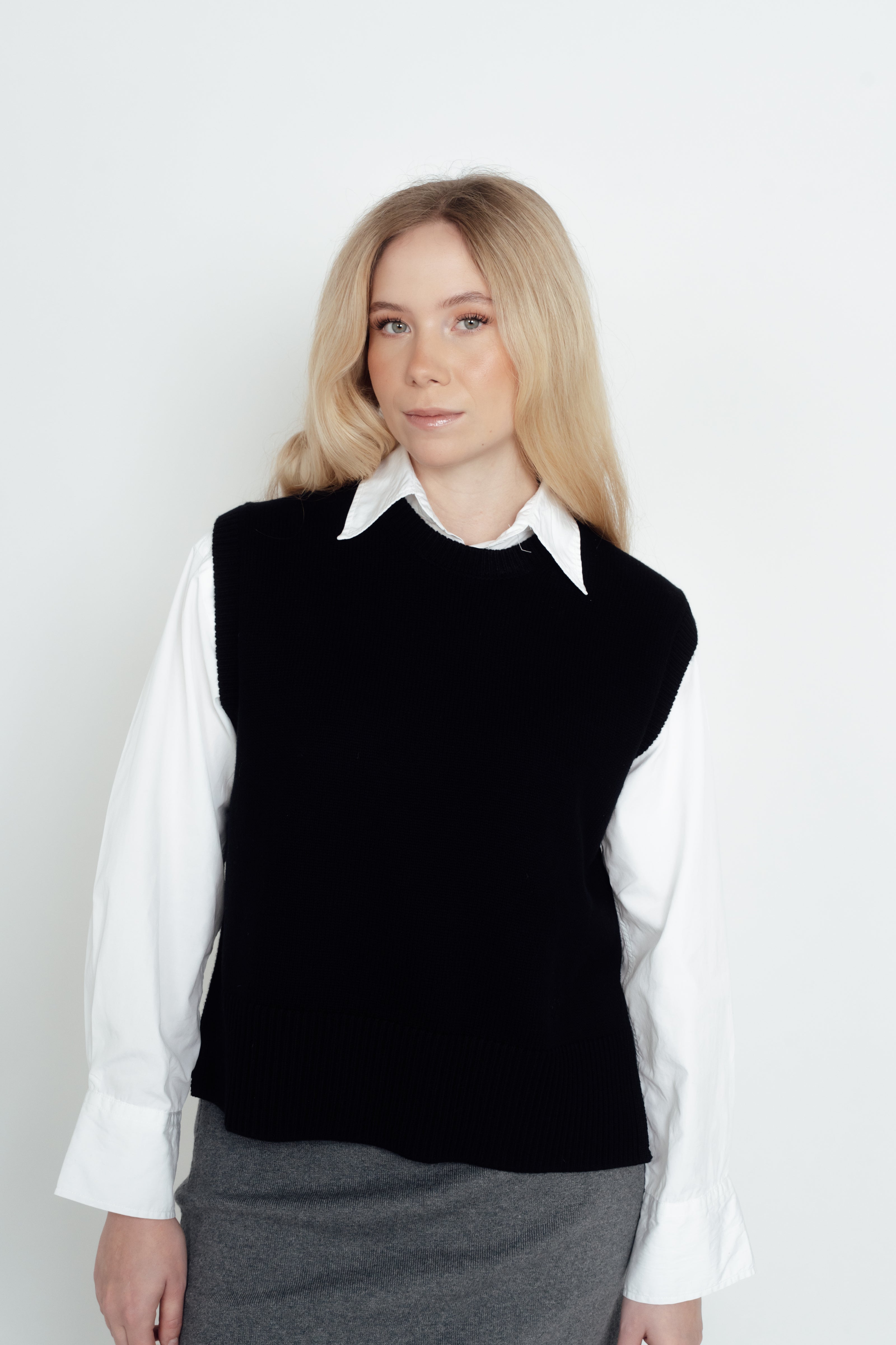 Video of a woman modelling the black CYME Merino Crewneck Vest over a white shirt with a black skirt and boots.