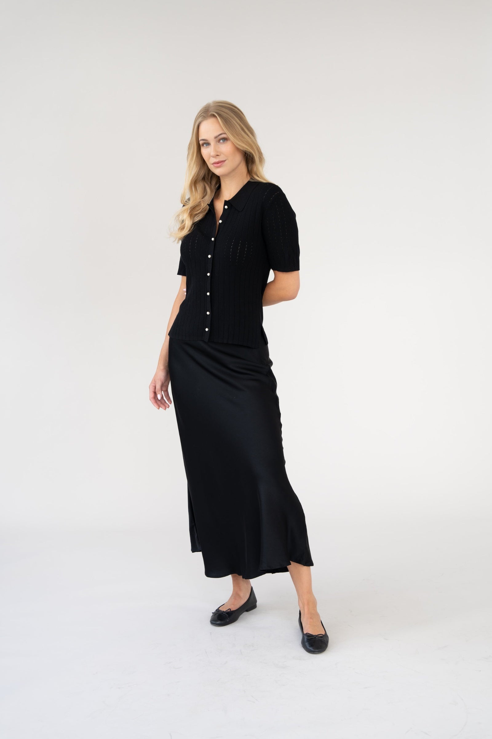 Woman wearing a satin skirt and a pointelle polo shirt in black.
