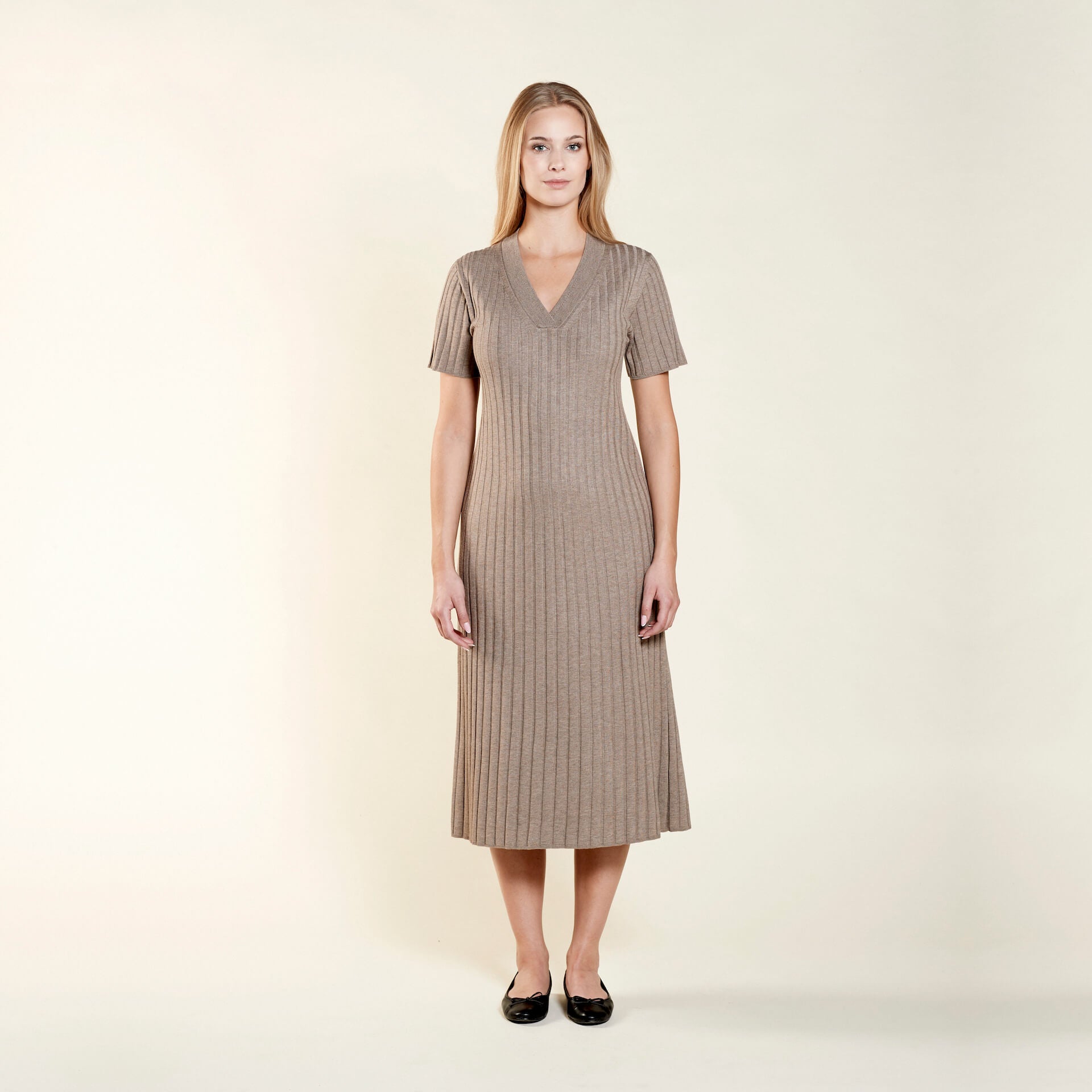 Smiling model presents a sophisticated V-neck knit dress by Cyme Copenhagen, crafted with natural materials, encapsulating the essence of sustainable, timeless Scandinavian fashion.