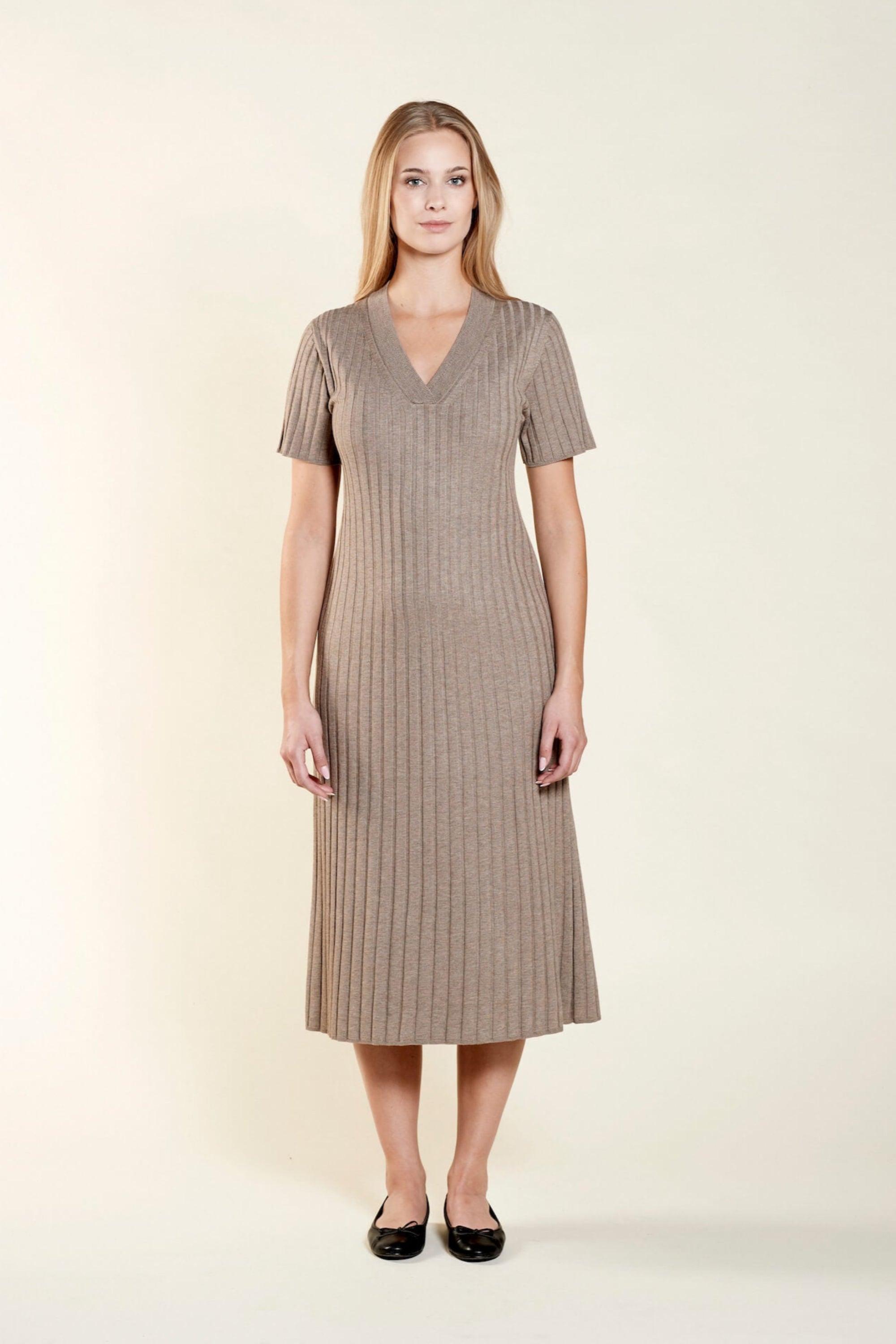 Smiling model presents a sophisticated V-neck knit dress by Cyme Copenhagen, crafted with natural materials, encapsulating the essence of sustainable, timeless Scandinavian fashion.