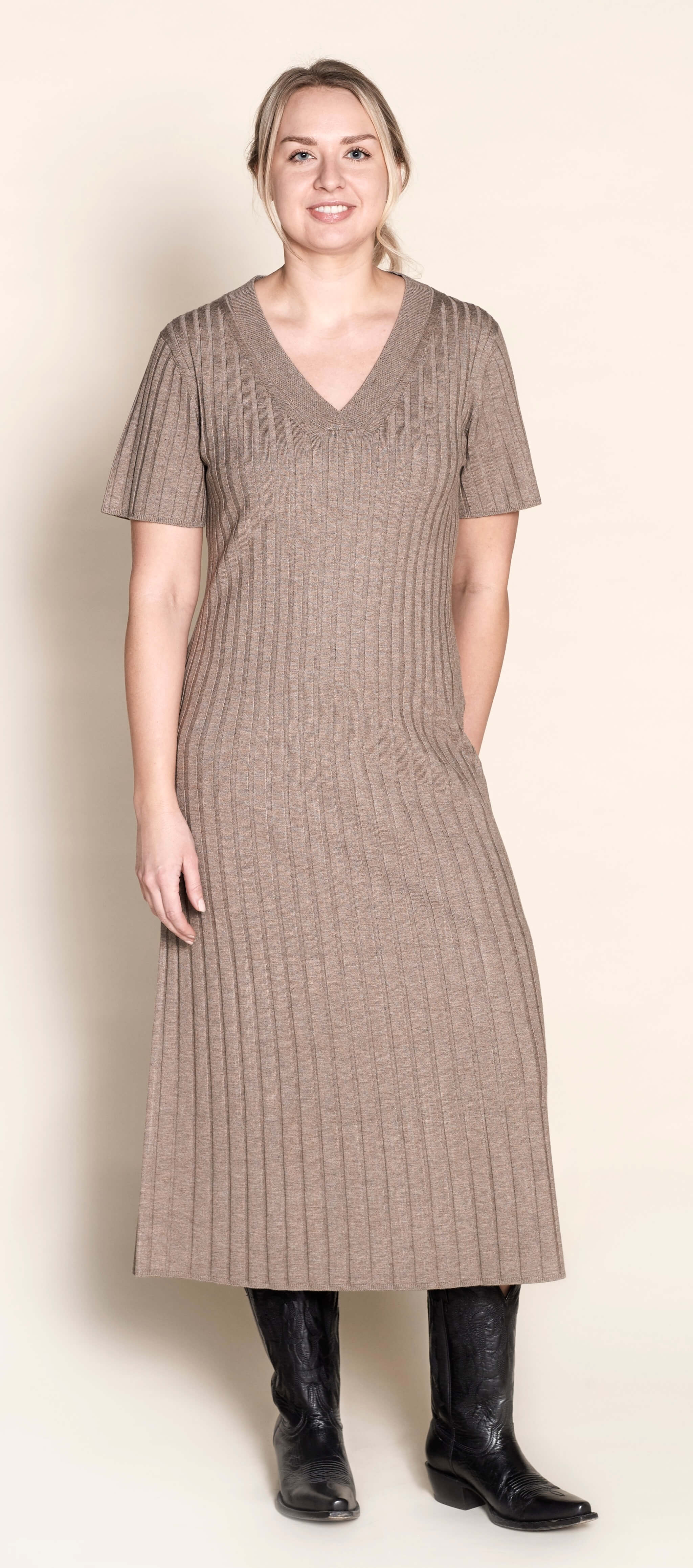 Smiling model presents a sophisticated V-neck knit dress by Cyme Copenhagen, crafted with natural materials, encapsulating the essence of sustainable, timeless Scandinavian fashion.