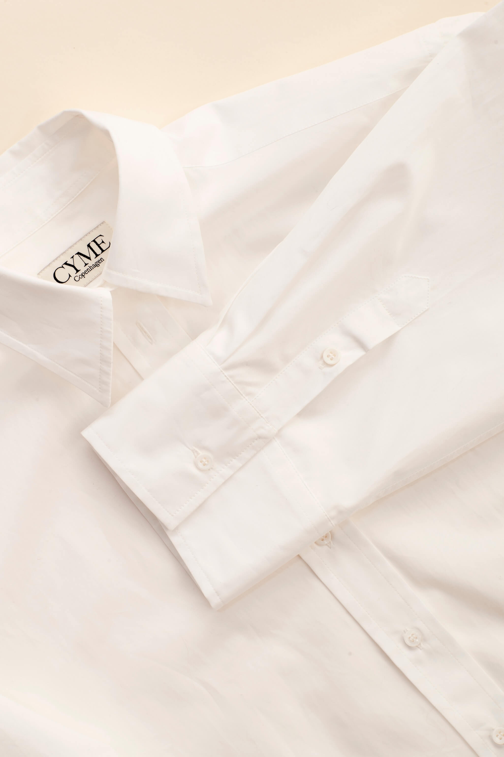 Detail of Cyme Copenhagen's minimalist white shirt with logo on the collar, embodying the clean and sustainable design of Scandinavian fashion.