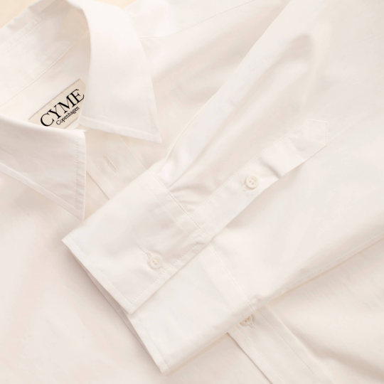 Showcasing the white supima shirt from CYME Copenhagen. Explore Cyme Copenhagen's Tops, where timeless design meets versatile style.