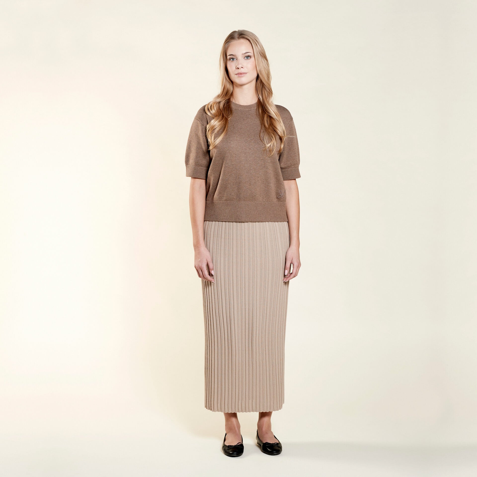 Confident model in a matching Cyme Copenhagen pointelle knit top and skirt set in soft beige, highlighting the brand's use of natural fibers for a sustainable and chic Scandinavian look.