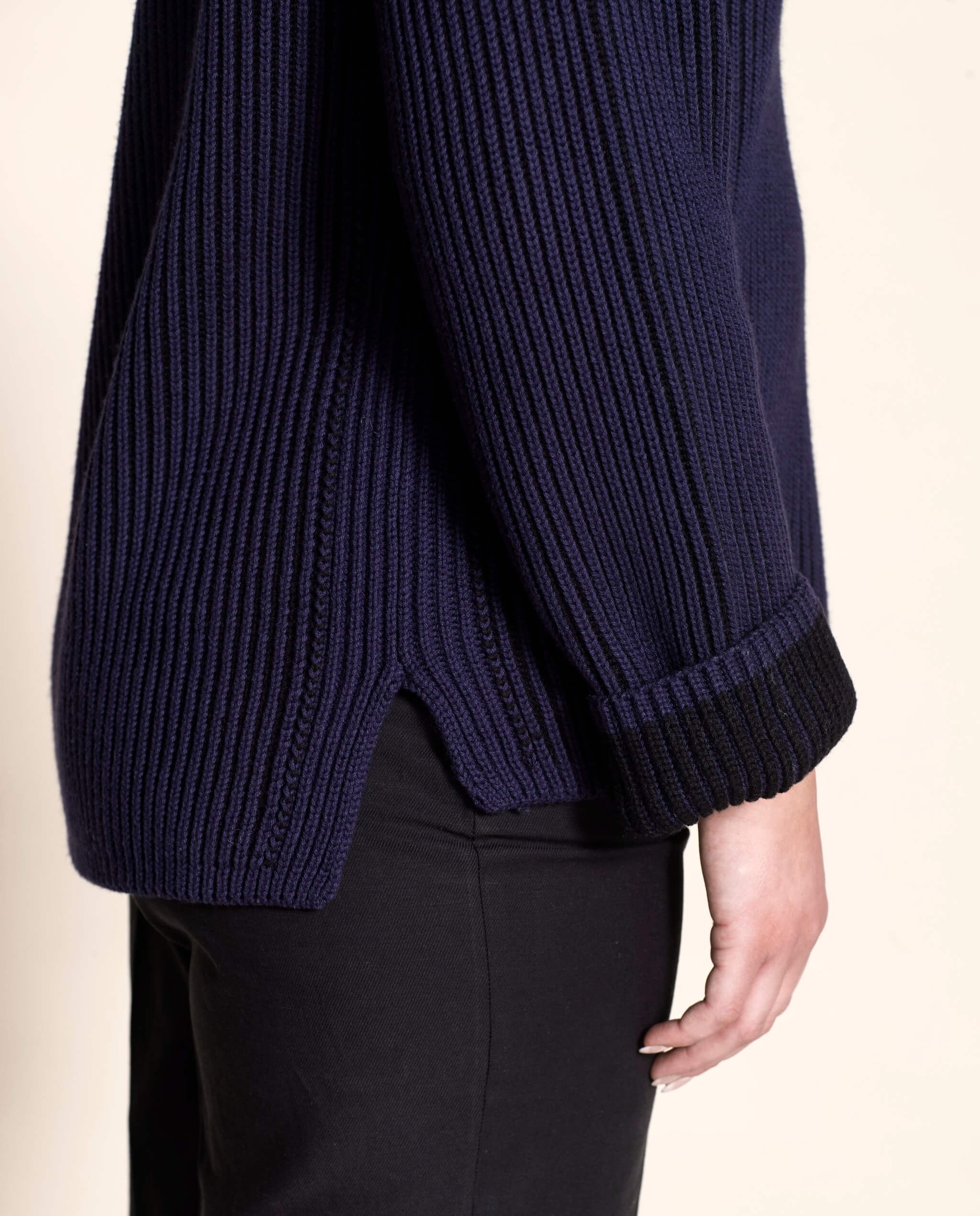 Detail of the side view of Cyme Copenhagen's navy ribbed sweater, featuring a high-low hem and textured knit, aligning with Scandinavian fashion trends and the brand's dedication to sustainable materials in women's clothing.