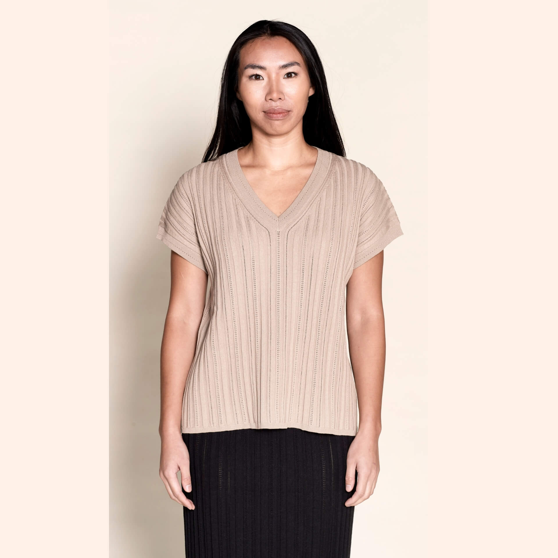 Model presents a taupe V-neck knit top by Cyme Copenhagen, exemplifying the blend of sustainable fashion with Danish designer expertise, available in a clothing store that caters to fashion-forward and plus-size women's clothes.