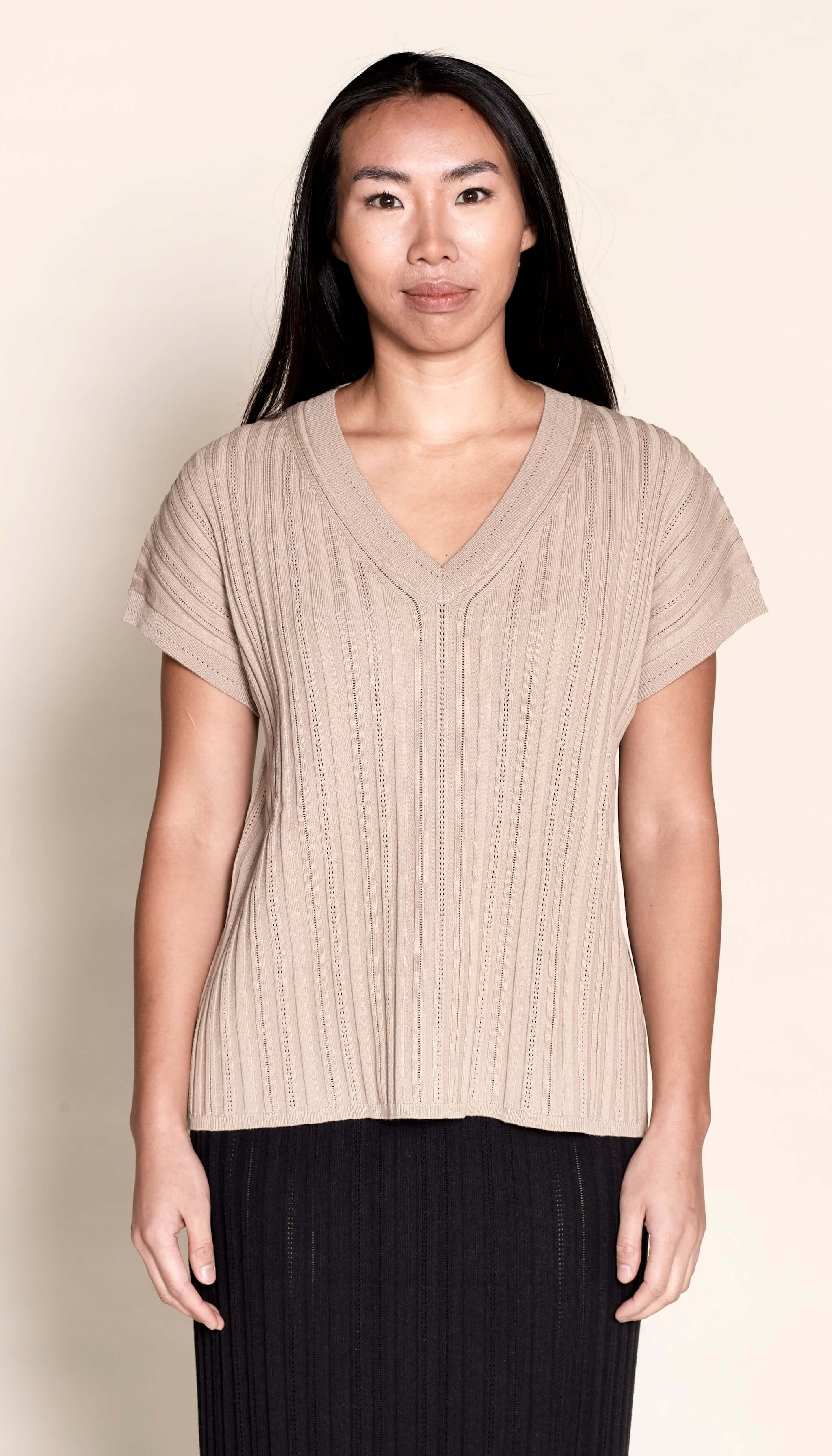 Model presents a taupe V-neck knit top by Cyme Copenhagen, exemplifying the blend of sustainable fashion with Danish designer expertise, available in a clothing store that caters to fashion-forward and plus-size women's clothes.