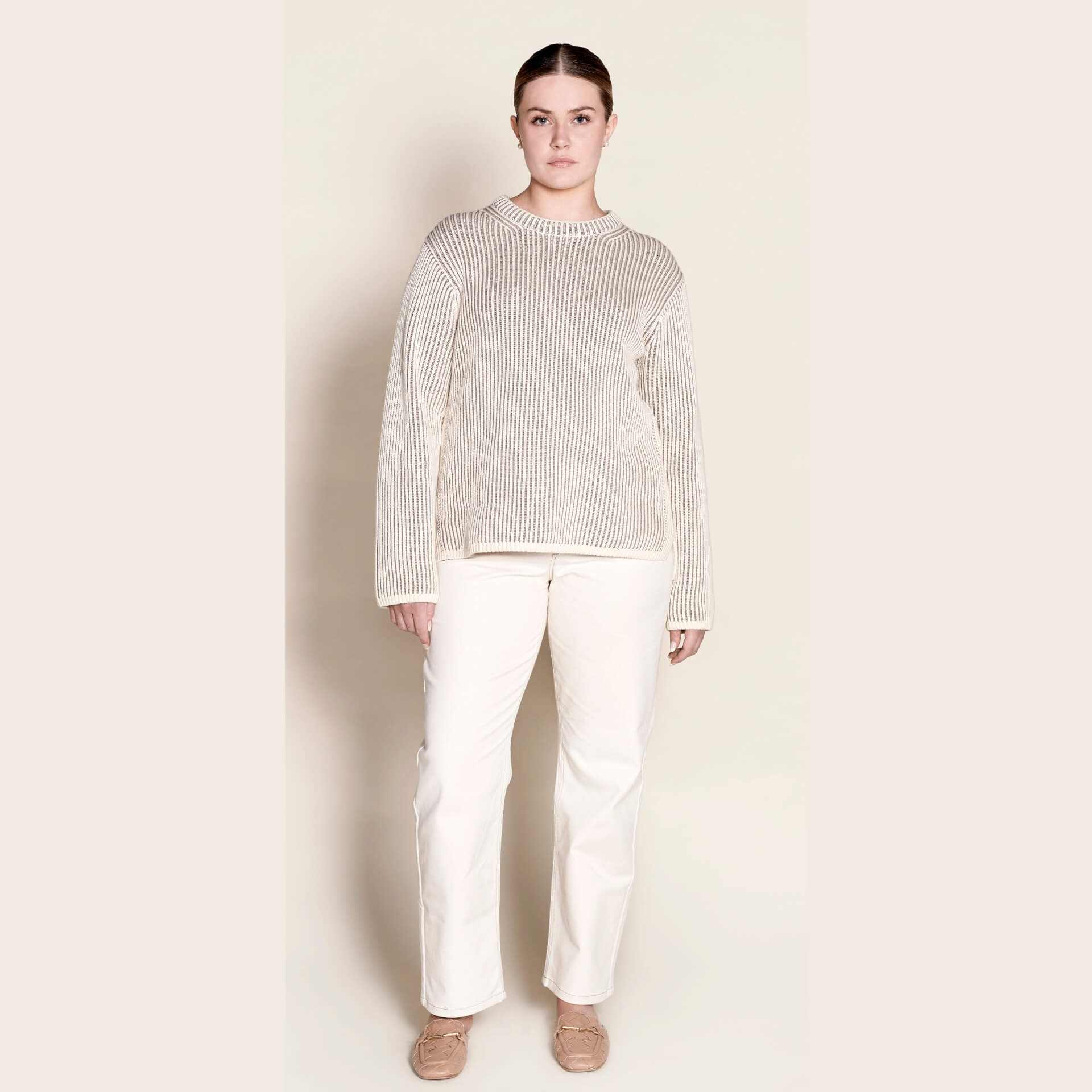 Model in a Cyme Copenhagen cream ribbed cashmere knit sweater paired with elegant white trousers, showcasing the brand's commitment to natural materials and sustainable, timeless women's fashion.