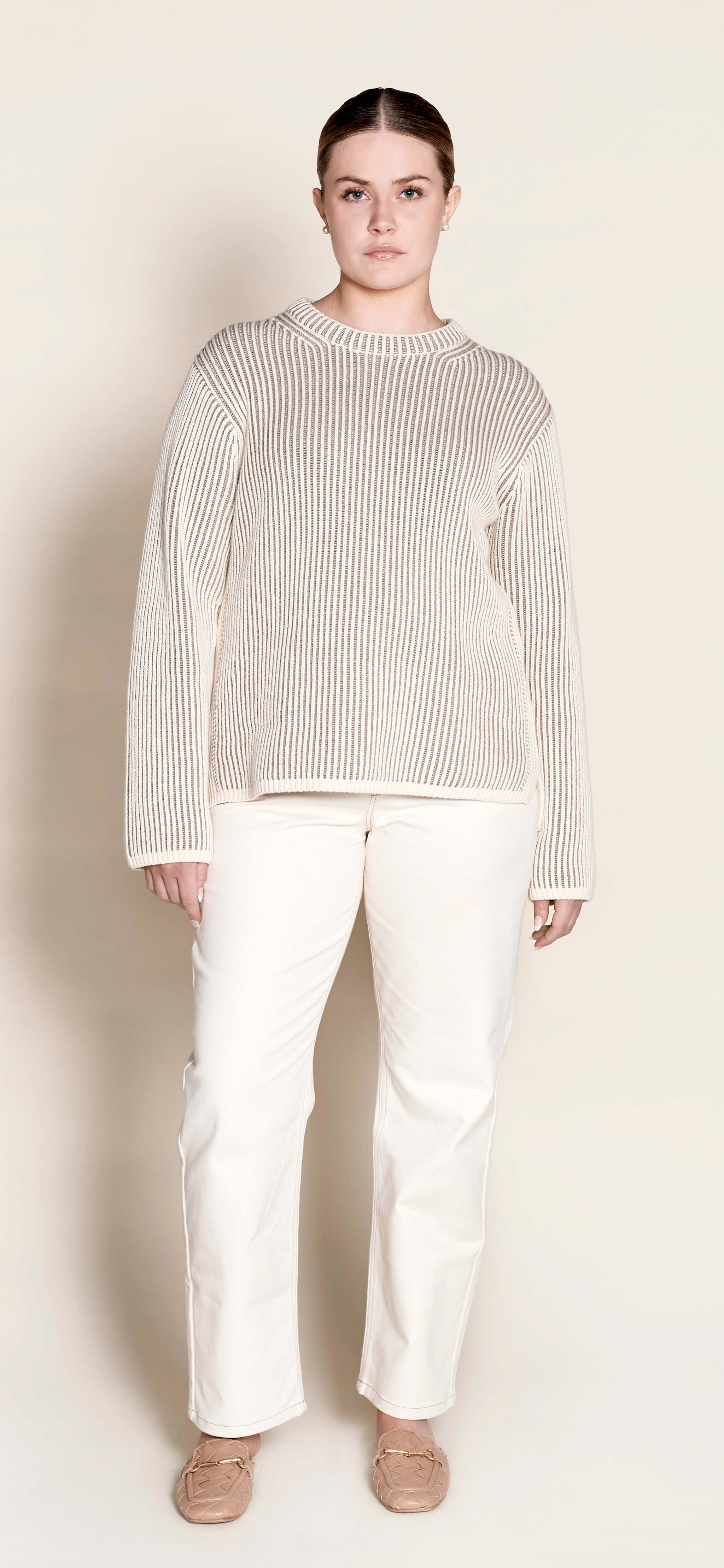 Model in a Cyme Copenhagen cream ribbed cashmere knit sweater paired with elegant white trousers, showcasing the brand's commitment to natural materials and sustainable, timeless women's fashion.