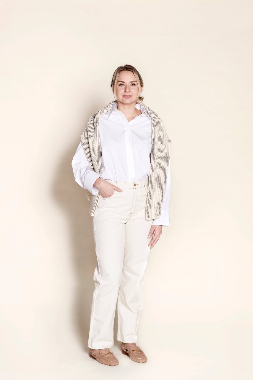 Casually elegant, a model wears Cyme Copenhagen's timeless white shirt and natural fabric trousers with the cyme sweater around the neck, highlighting sustainable fashion and Scandinavian design with a classic touch.