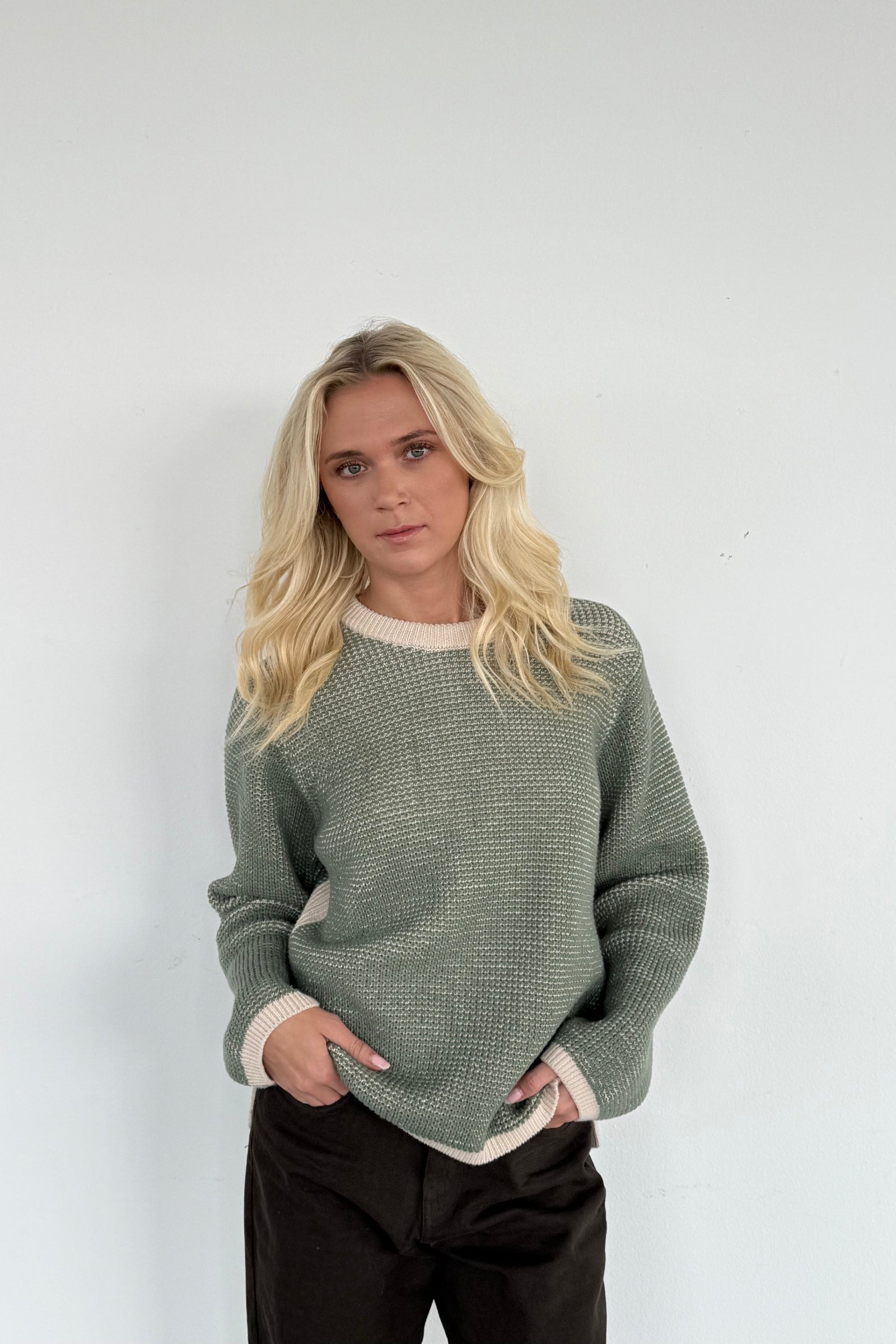 Person wearing a green sweater with a white collar against a plain background