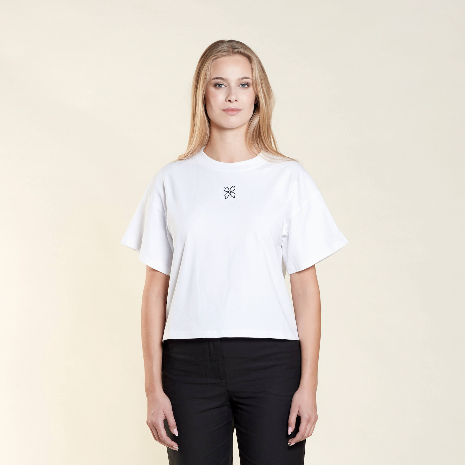 Woman wearing a white t-shirt from Cyme Copenhagen's spring/summer collection. The t-shirt features a simple design with a black logo in the center. The model stands against a neutral background, highlighting the minimalist and stylish appeal of the garment.