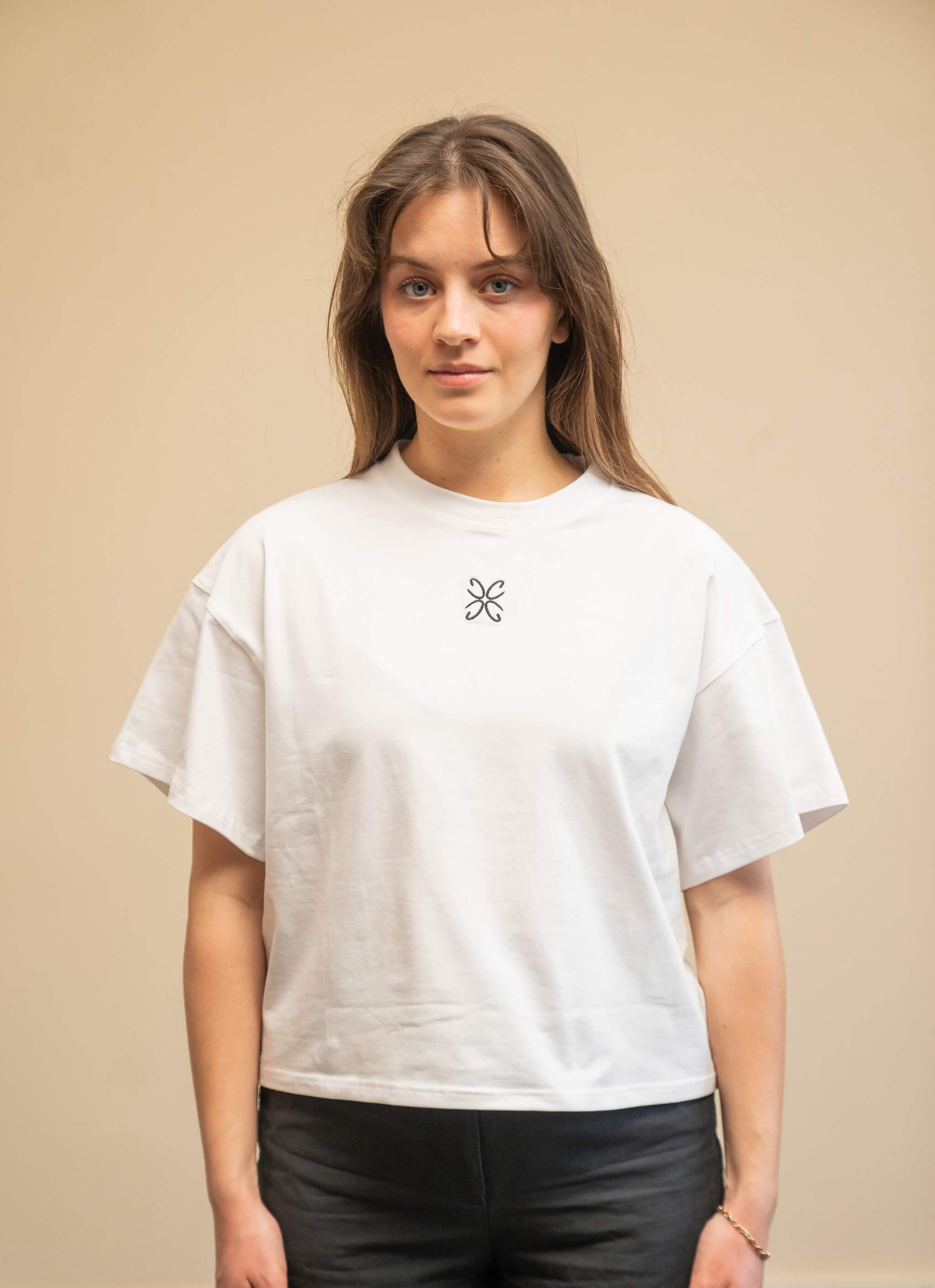 Woman wearing a white t-shirt from Cyme Copenhagen's spring/summer collection. The t-shirt features a simple design with a black logo in the center. The model stands against a neutral background, highlighting the minimalist and stylish appeal of the garment.